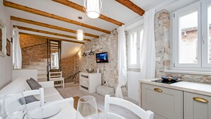A modern kitchen with a stone wall, wooden beams, and a dining area with white furniture. - Apartment and Studio CA 3 VIE (Rovinj)