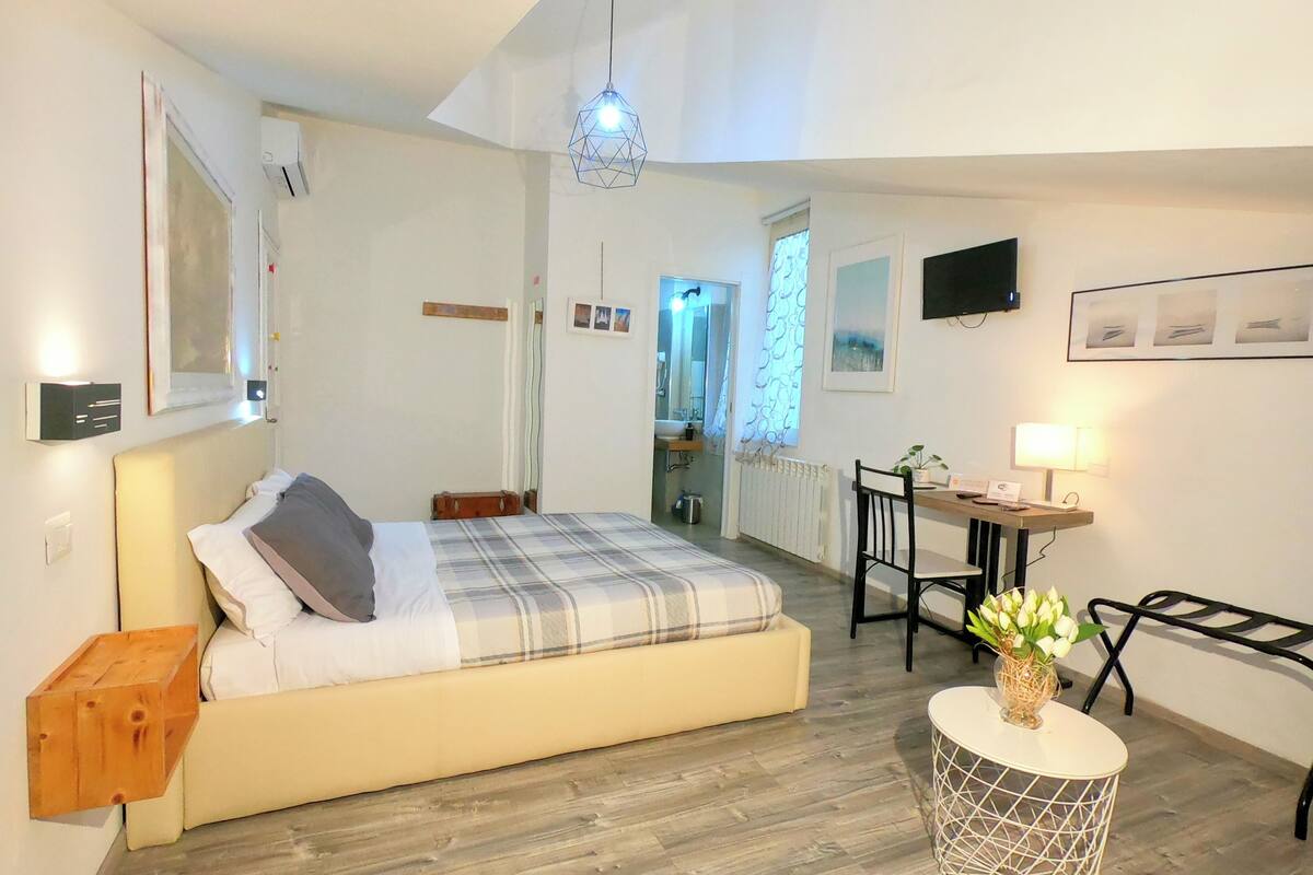 A bedroom with a bed, bedside table, wooden floor, and a small round table with a vase of flowers.