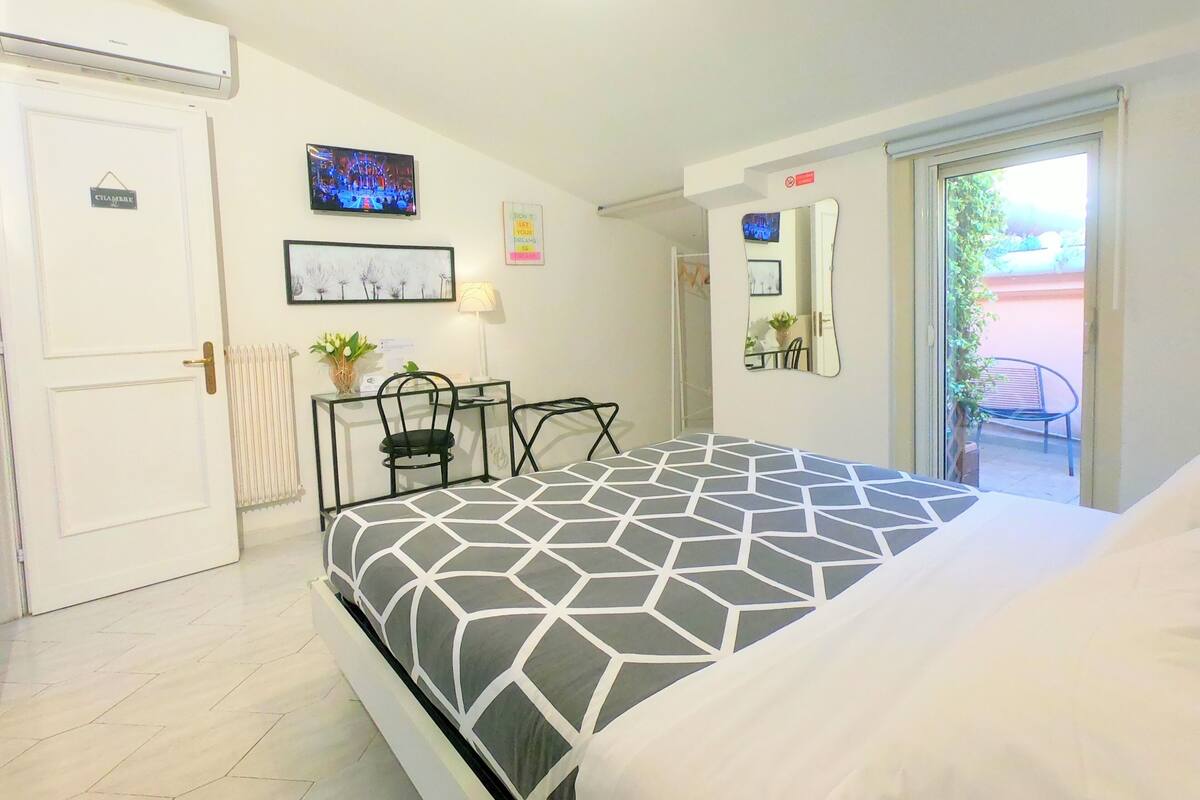 A bedroom with a bed, a desk, a chair, a radiator, a TV, and a door.
