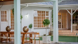 Een zwembadgedeelte met een houten tafel en stoelen, een kleine tuin en een wit gebouw met ramen.