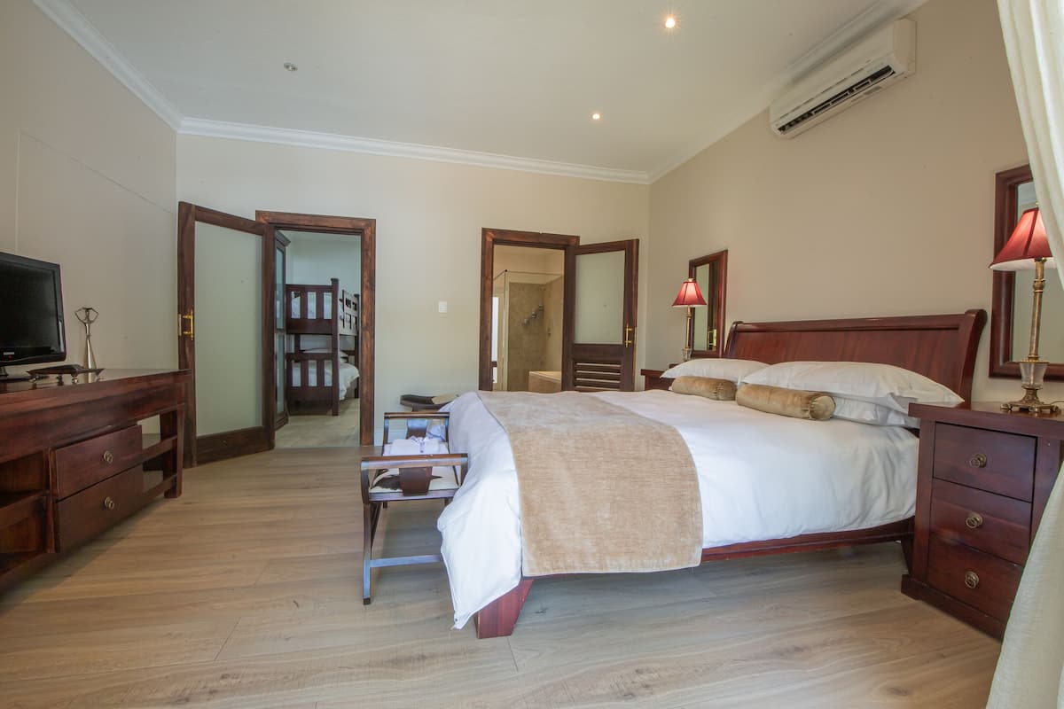 A bedroom with a wooden bed, bedside tables, a TV, and an air conditioning unit.