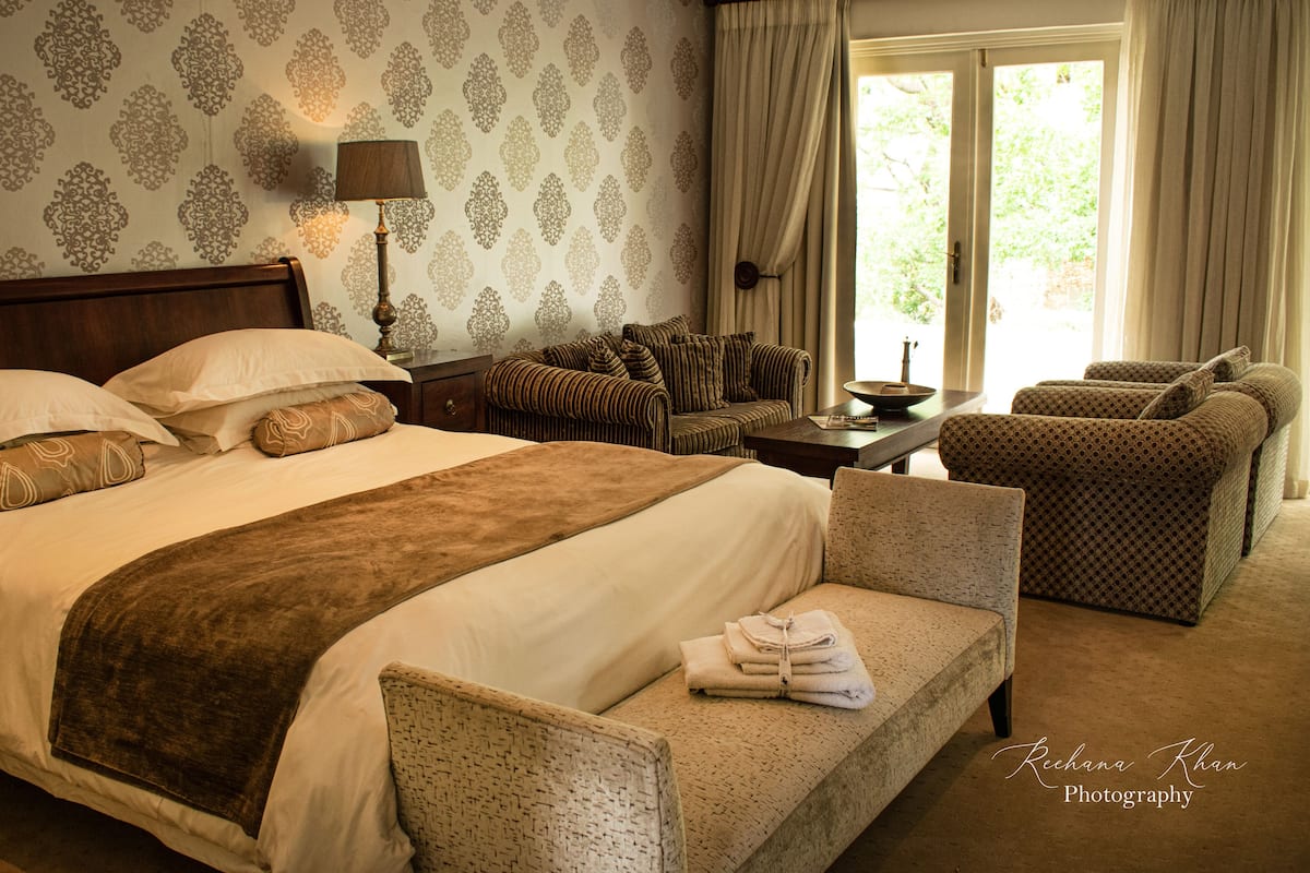 A hotel room with a large bed, a sitting area with two chairs, a small table, and a window with curtains.