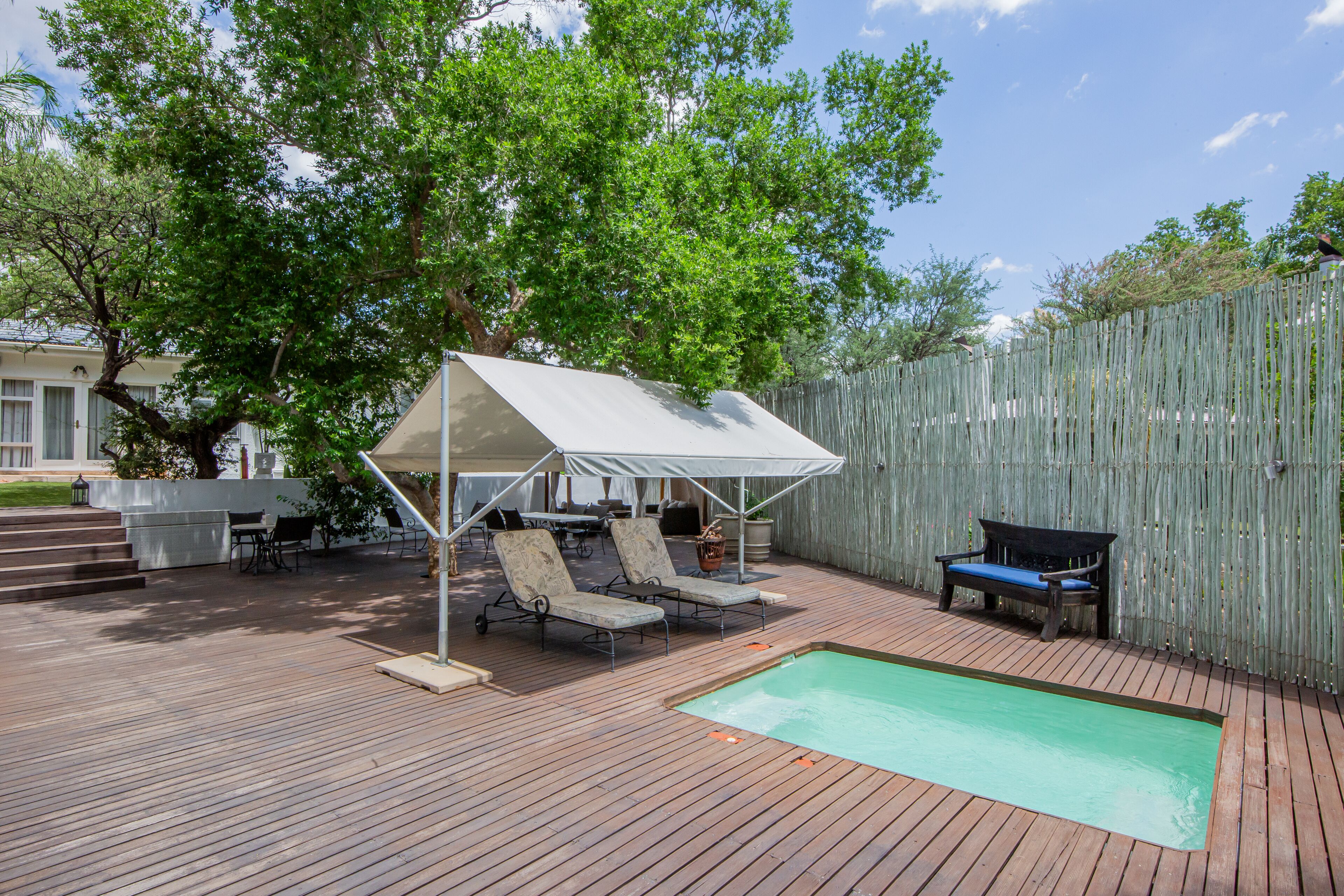 A wooden deck with a pool, lounge chairs, and a covered seating area.