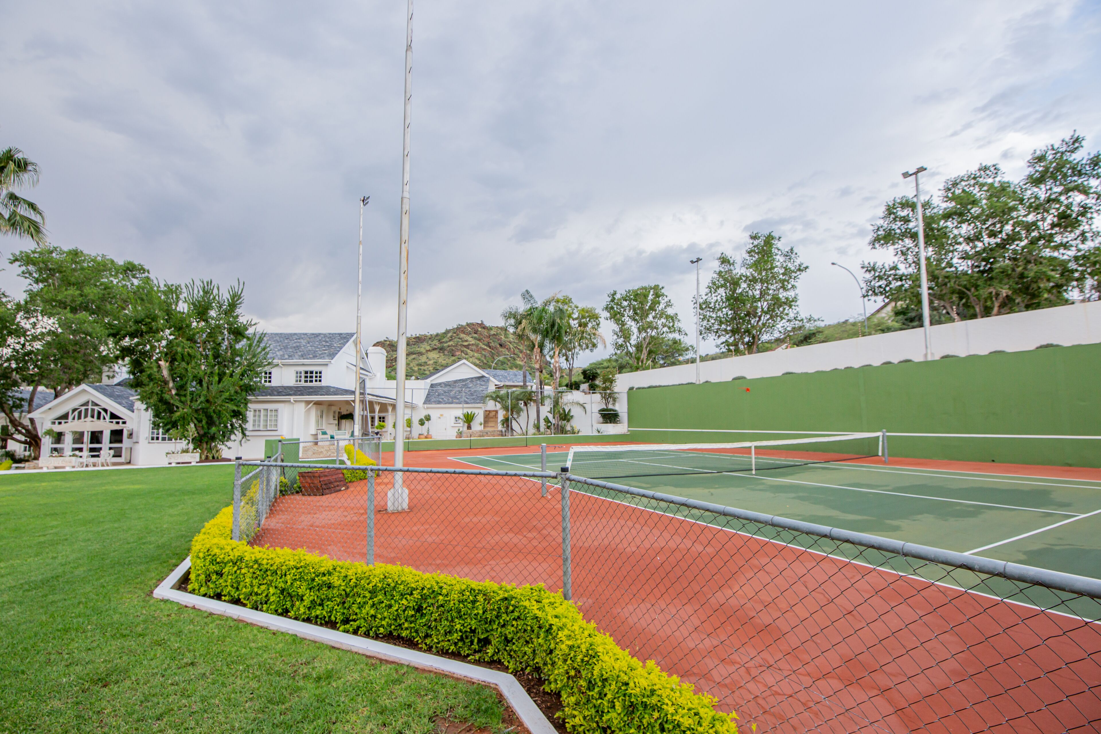 A tennis court with a fence, a flagpole, and a building in the background.