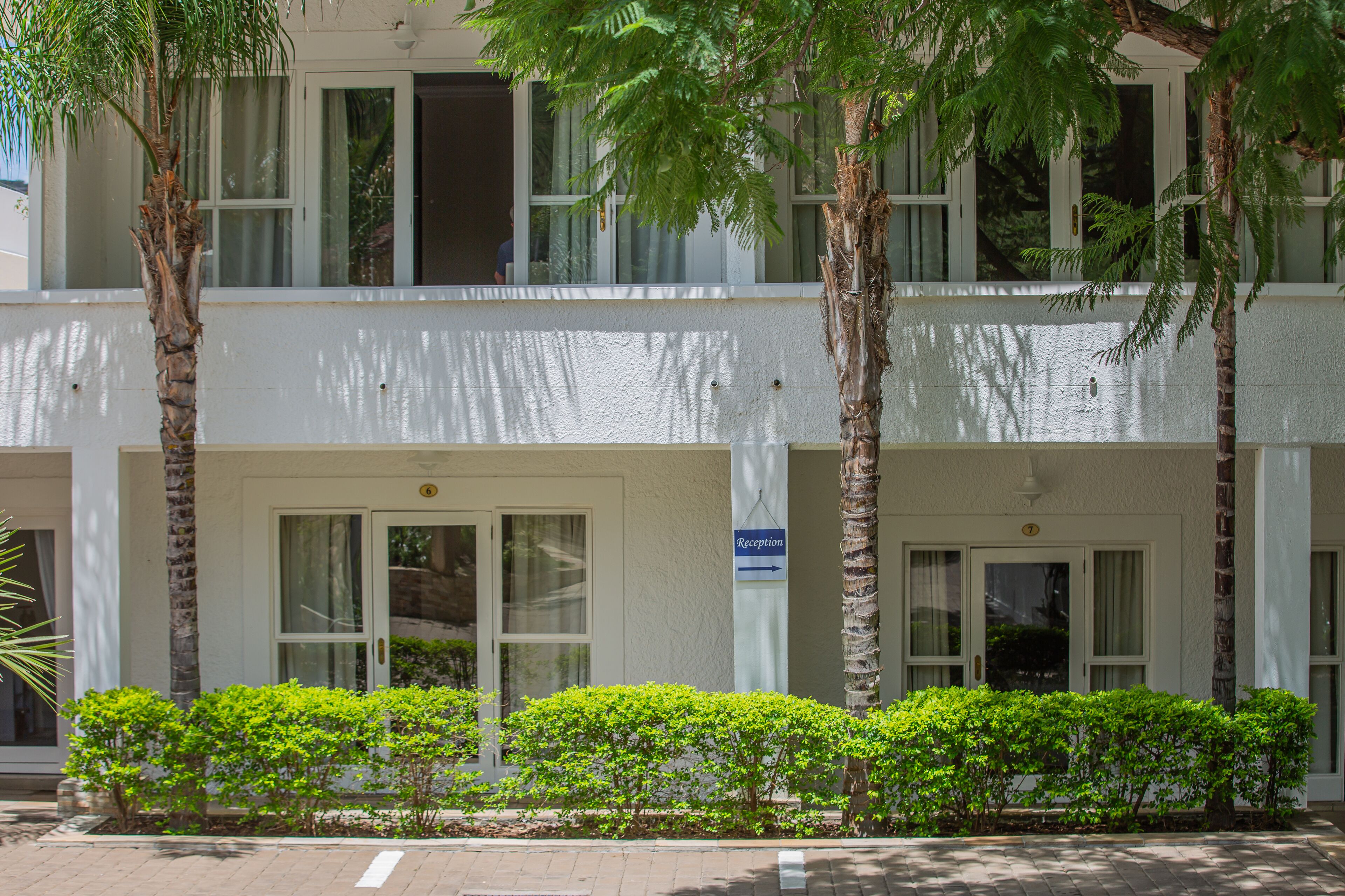 A two-story building with a reception sign, palm trees, and a well-maintained hedge.