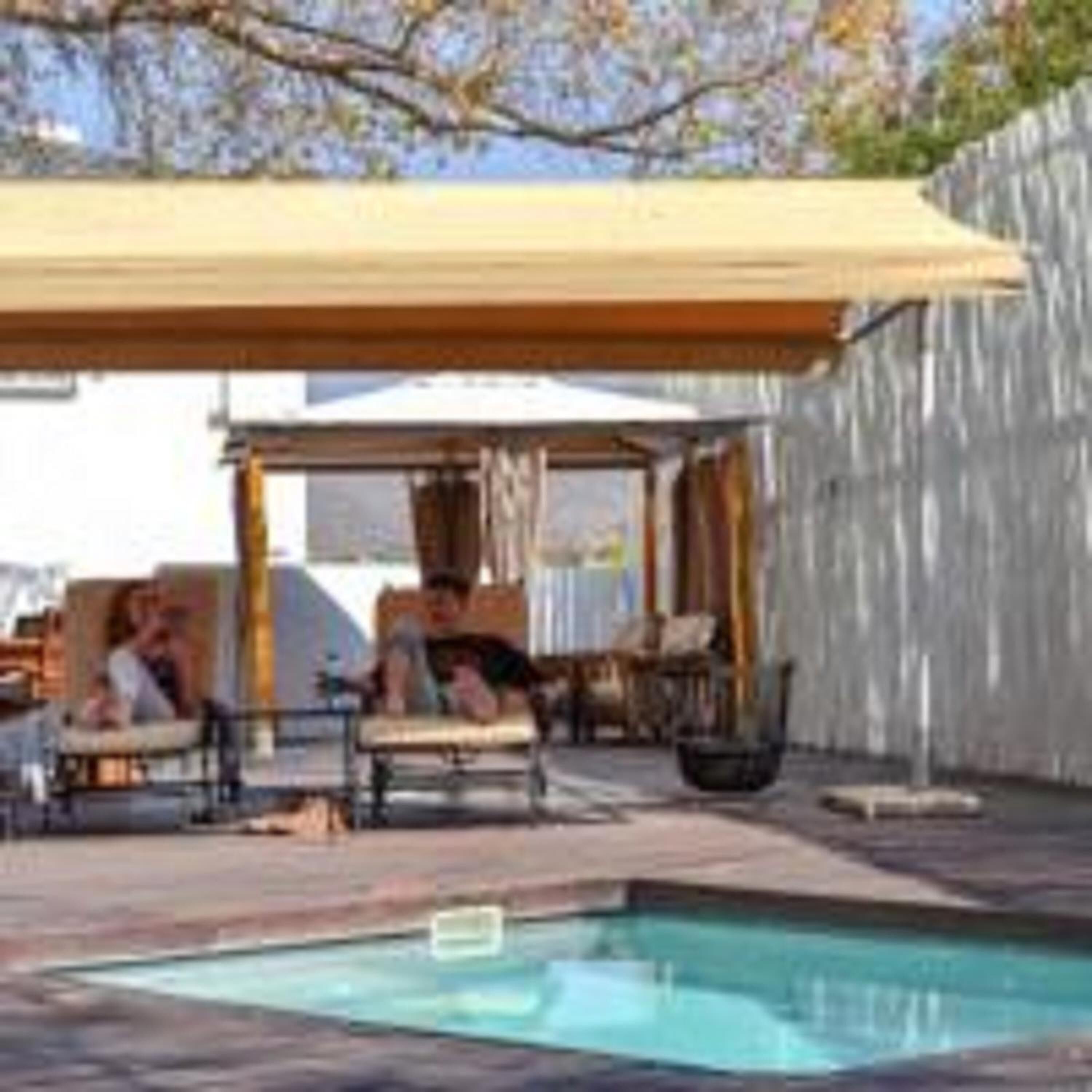 A pool area with a covered seating area and a view of a house in the background.