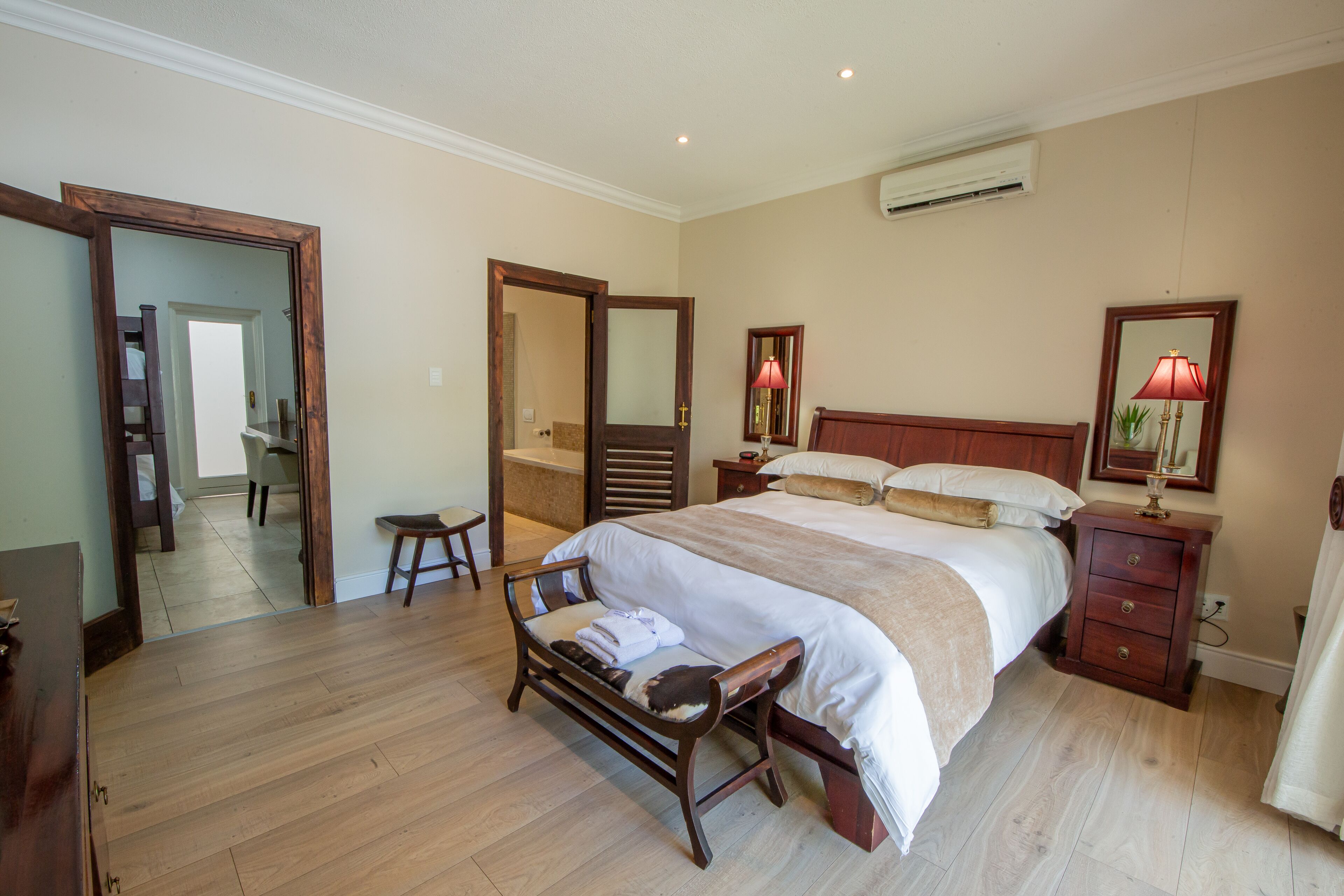 Un dormitorio con una cama grande, muebles de madera, un banco, una mesita de noche y un espejo.