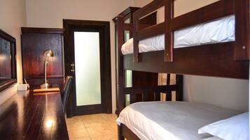 A room with a bunk bed, a desk with a lamp, and a door leading to another room.