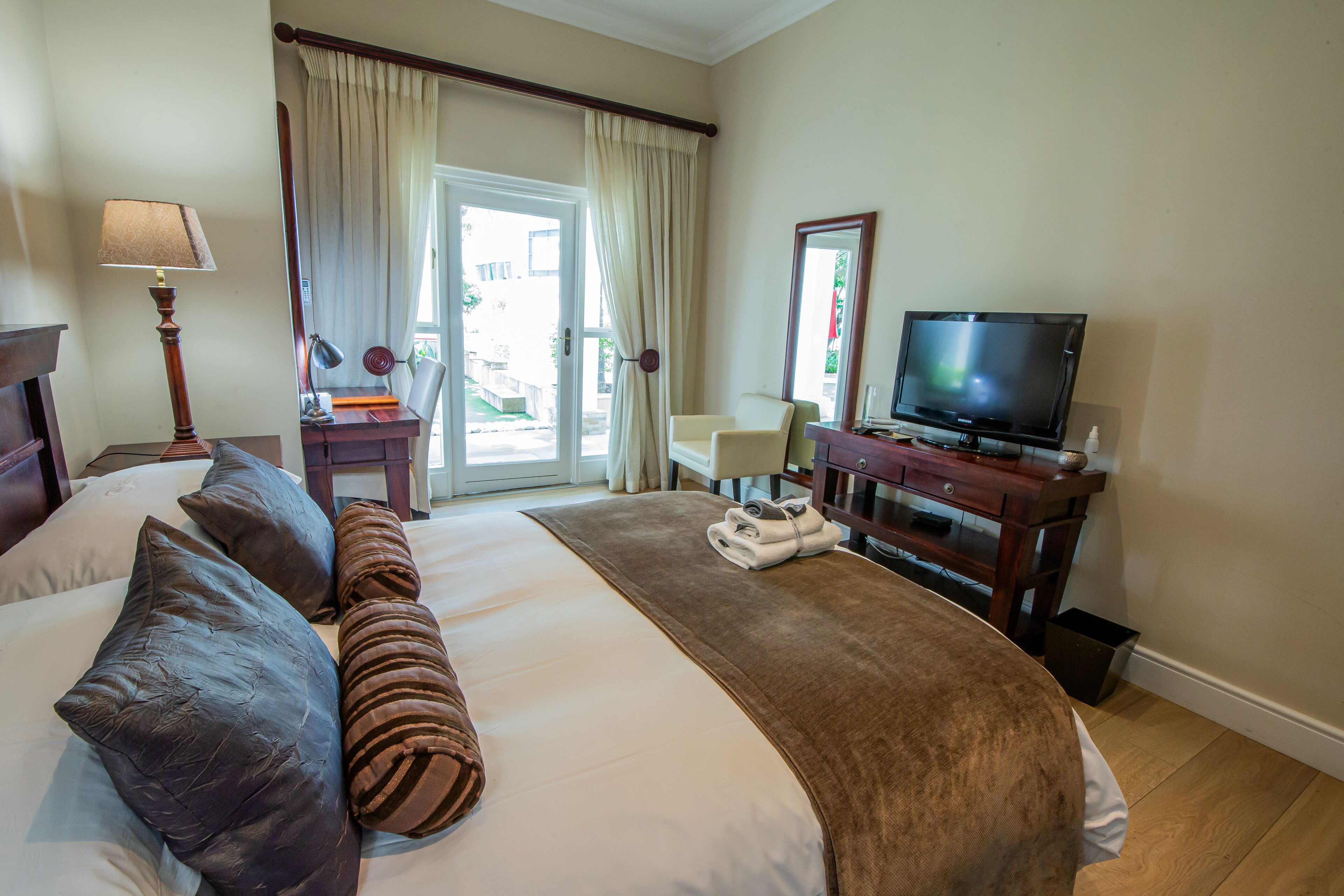 A hotel room with a large bed, a television, a desk with a lamp, and a chair near a window.
