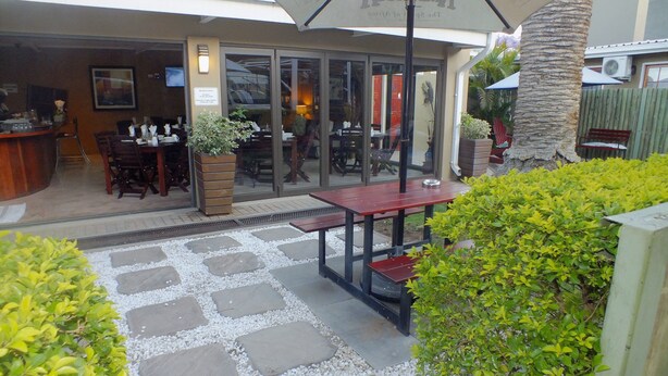 An outdoor patio area with stone flooring, a wooden table, and a large umbrella. - Uzuri Guesthouse (Windhoek)