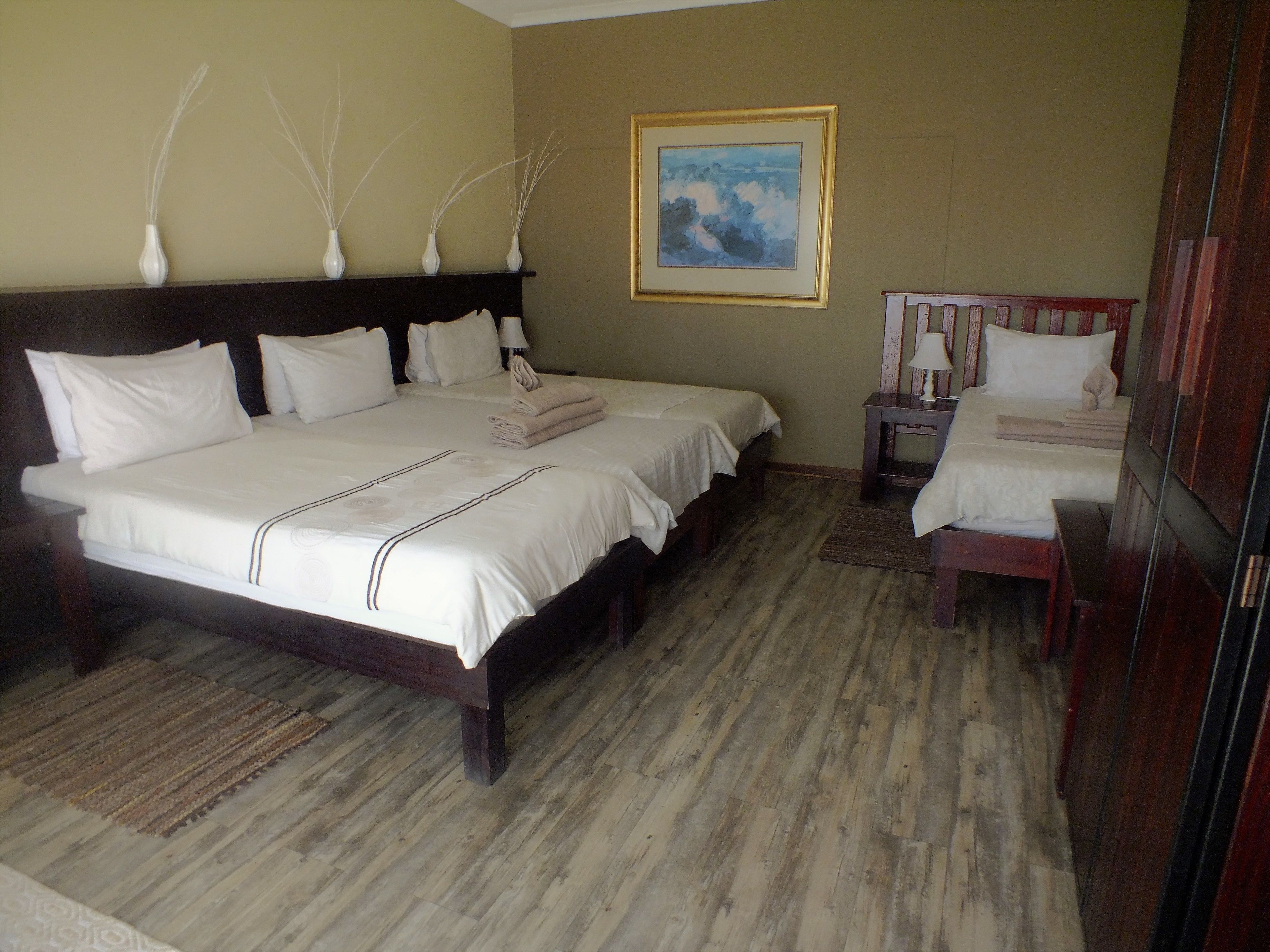 Una habitación de hotel con una cama grande, una cama más pequeña, una mesita de noche, una silla y un cuadro en la pared.