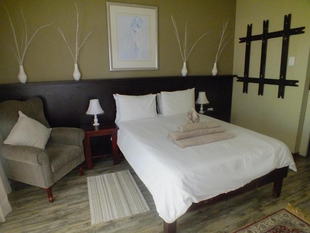 A hotel room with a bed, a chair, a nightstand, a lamp, and decorative wall art.
