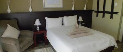 A hotel room with a bed, a chair, a nightstand, a lamp, and decorative wall art.