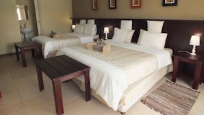 A hotel room with two beds, a small table, bedside lamps, and a rug. - Uzuri Guesthouse (Windhoek)