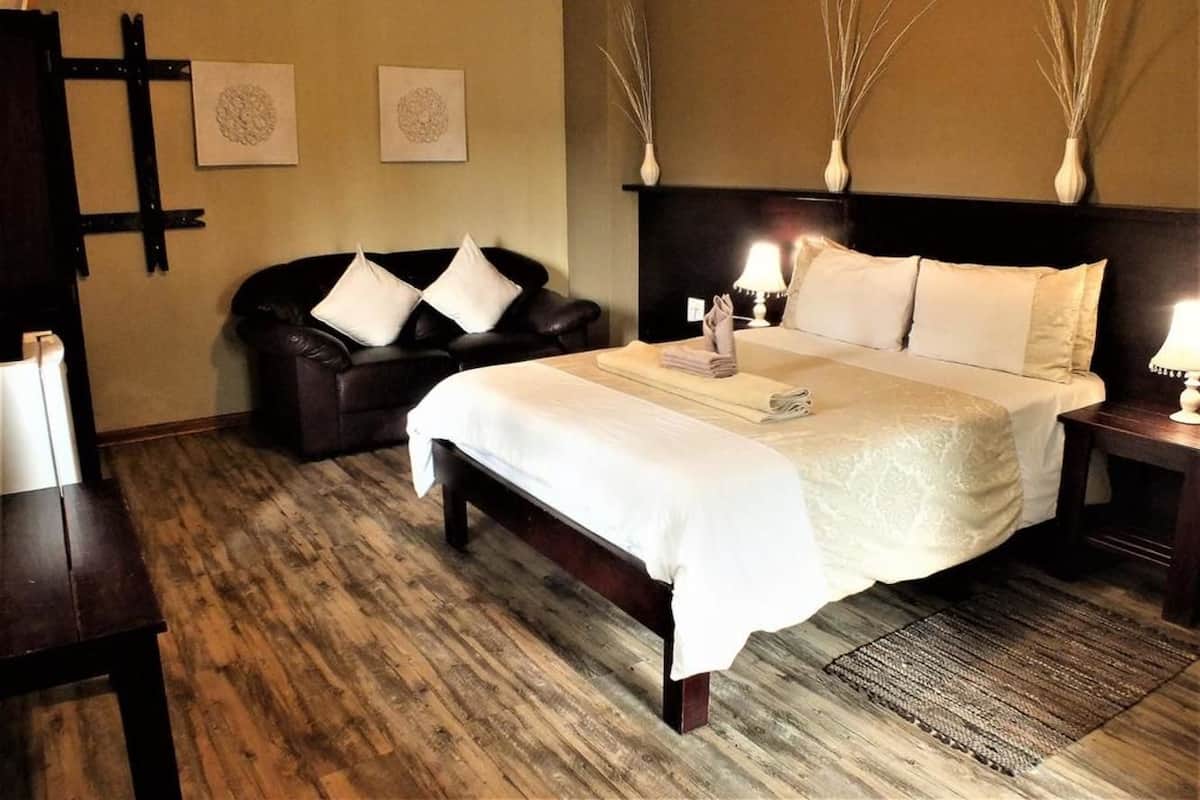 Ein Hotelzimmer mit einem großen Bett, einem dunklen Ledersofa, Holzboden und zwei an der Wand befestigten Vasen.