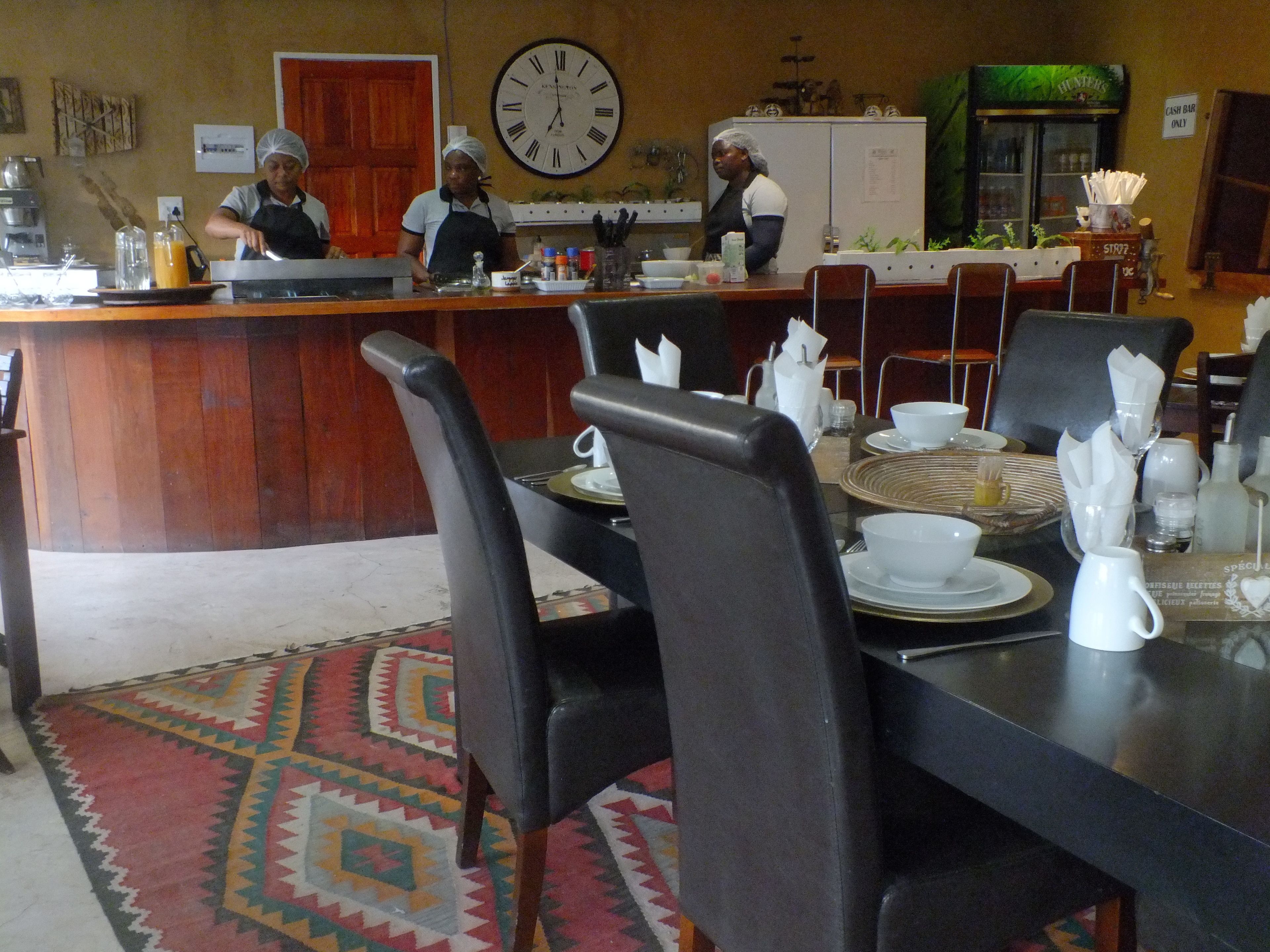 Ein Restaurant mit einer Holztheke, schwarzen Stühlen und einer Uhr an der Wand.