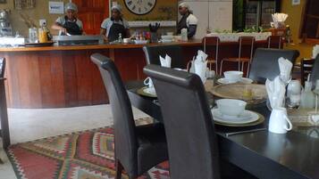 A restaurant with a wooden counter, black chairs, and a clock on the wall.