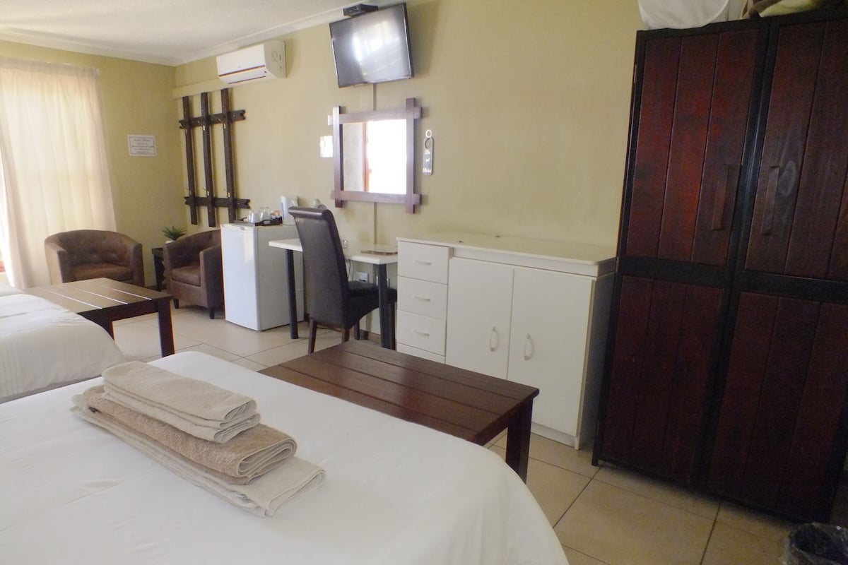 Ein Hotelzimmer mit zwei Betten, einem Schreibtisch, einem Stuhl, einem Fernseher und einem Kleiderschrank.