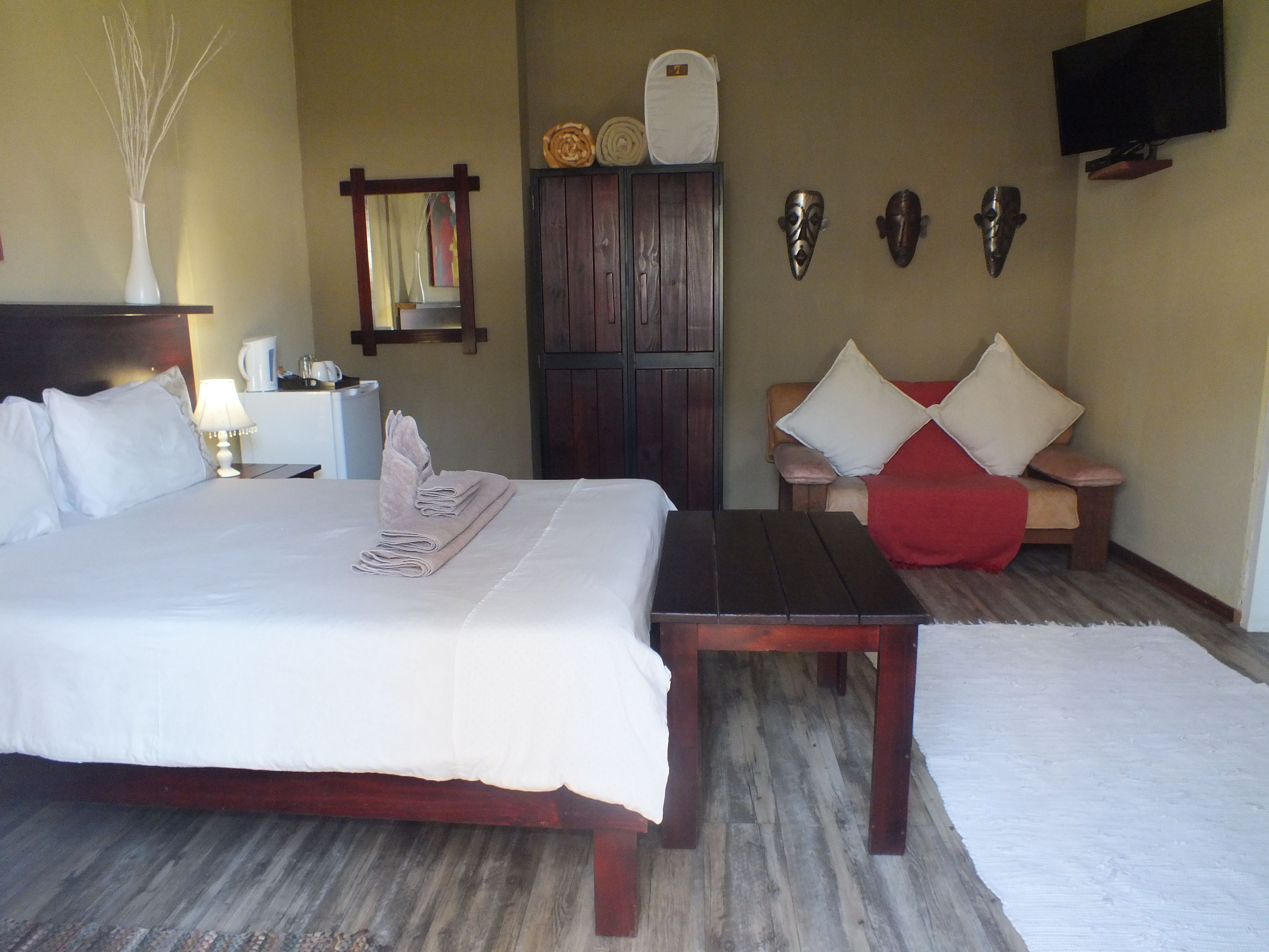 Une chambre d’hôtel avec un grand lit, une table de chevet en bois, un bureau, un canapé et un téléviseur fixé au mur.