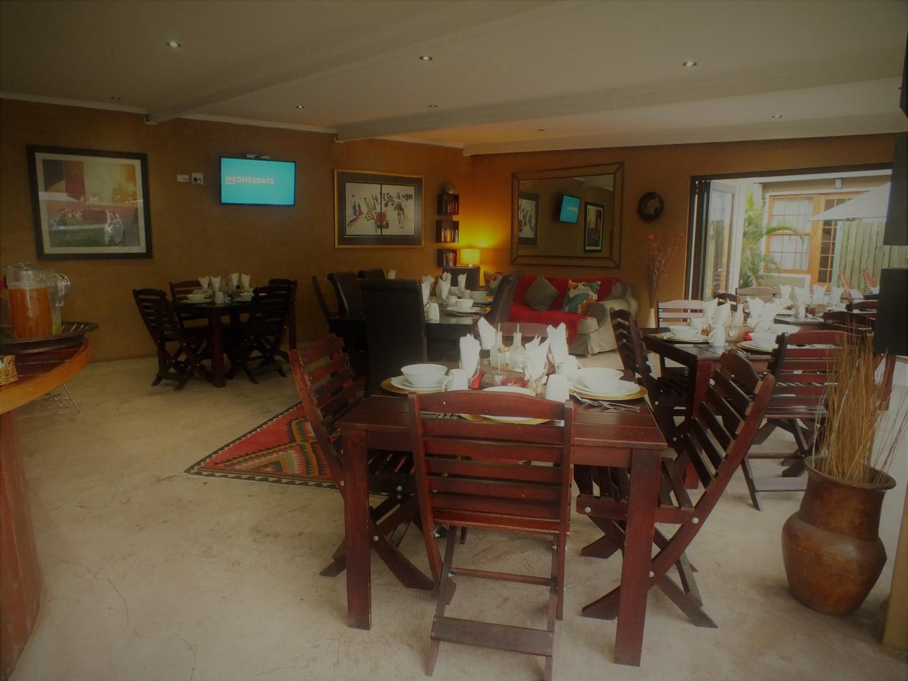 A dining area with wooden tables and chairs, a television mounted on the wall, and framed artwork on the walls.