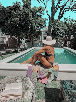 A person sitting by a pool with a book, surrounded by greenery and a building in the background. - Linda Vista (Cape Town)