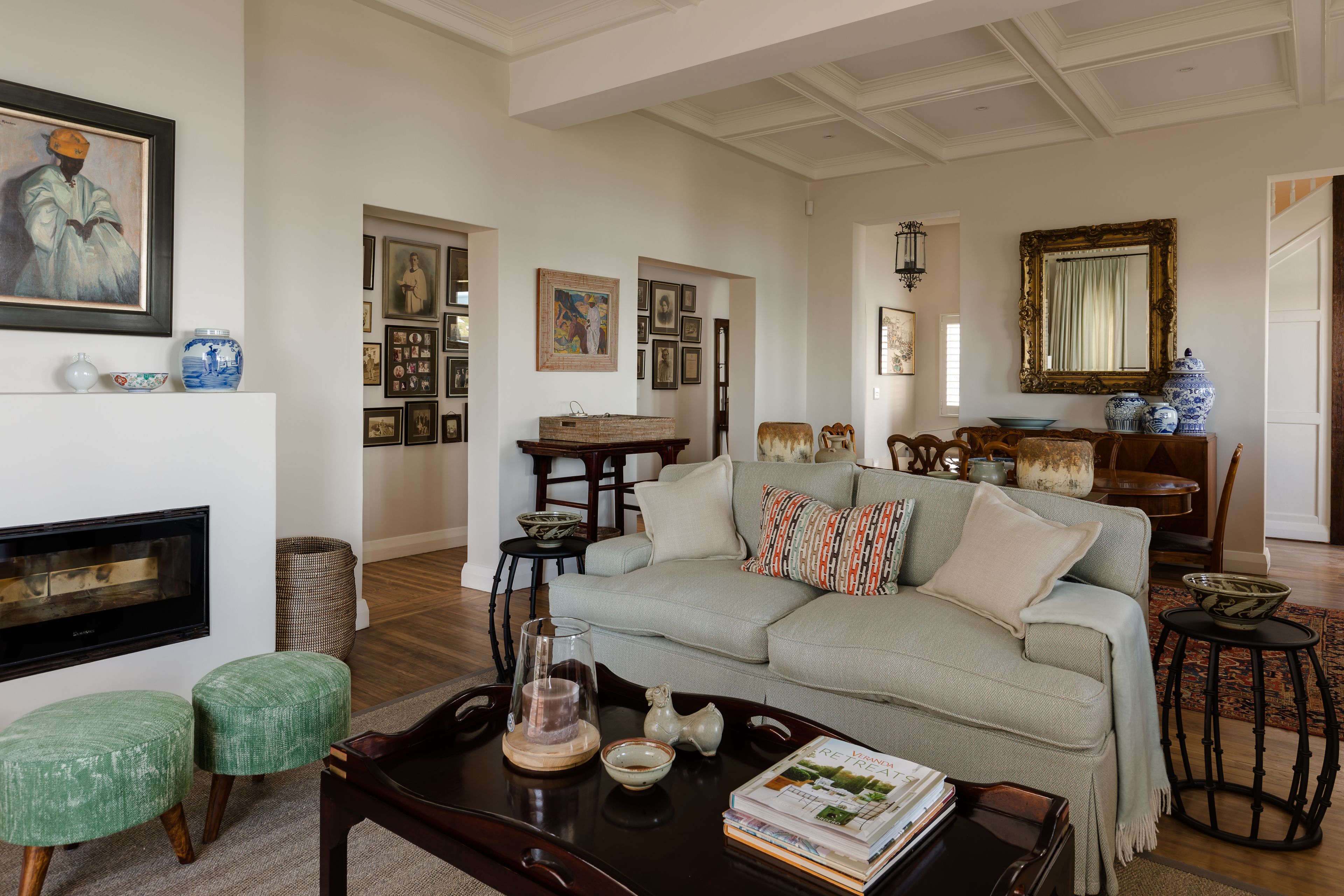 A living room with a sofa, coffee table, and a fireplace. There are framed pictures on the walls and a mirror above the sofa.