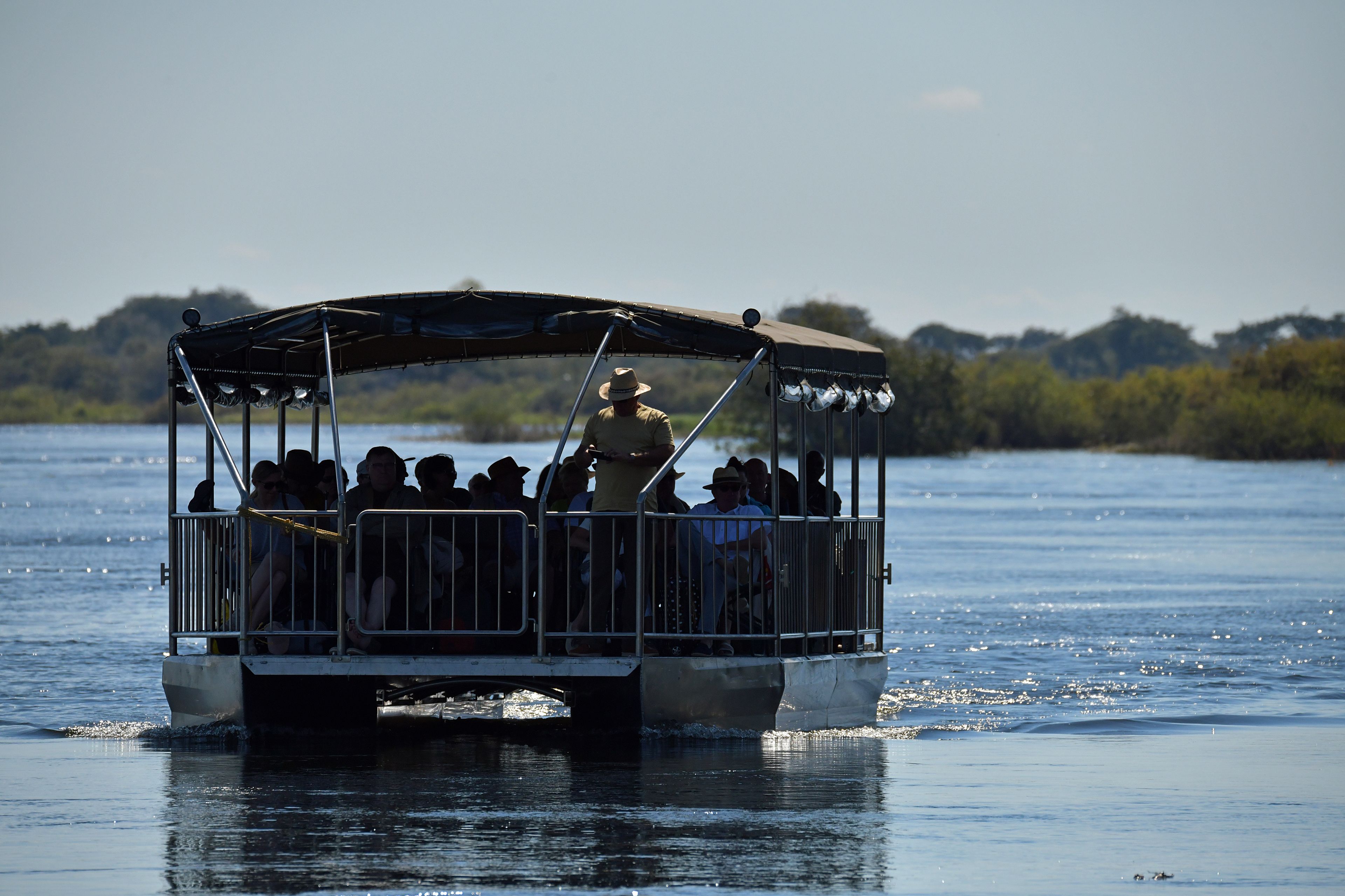 A boat with a covered deck and metal railings, carrying passengers on a body of water.