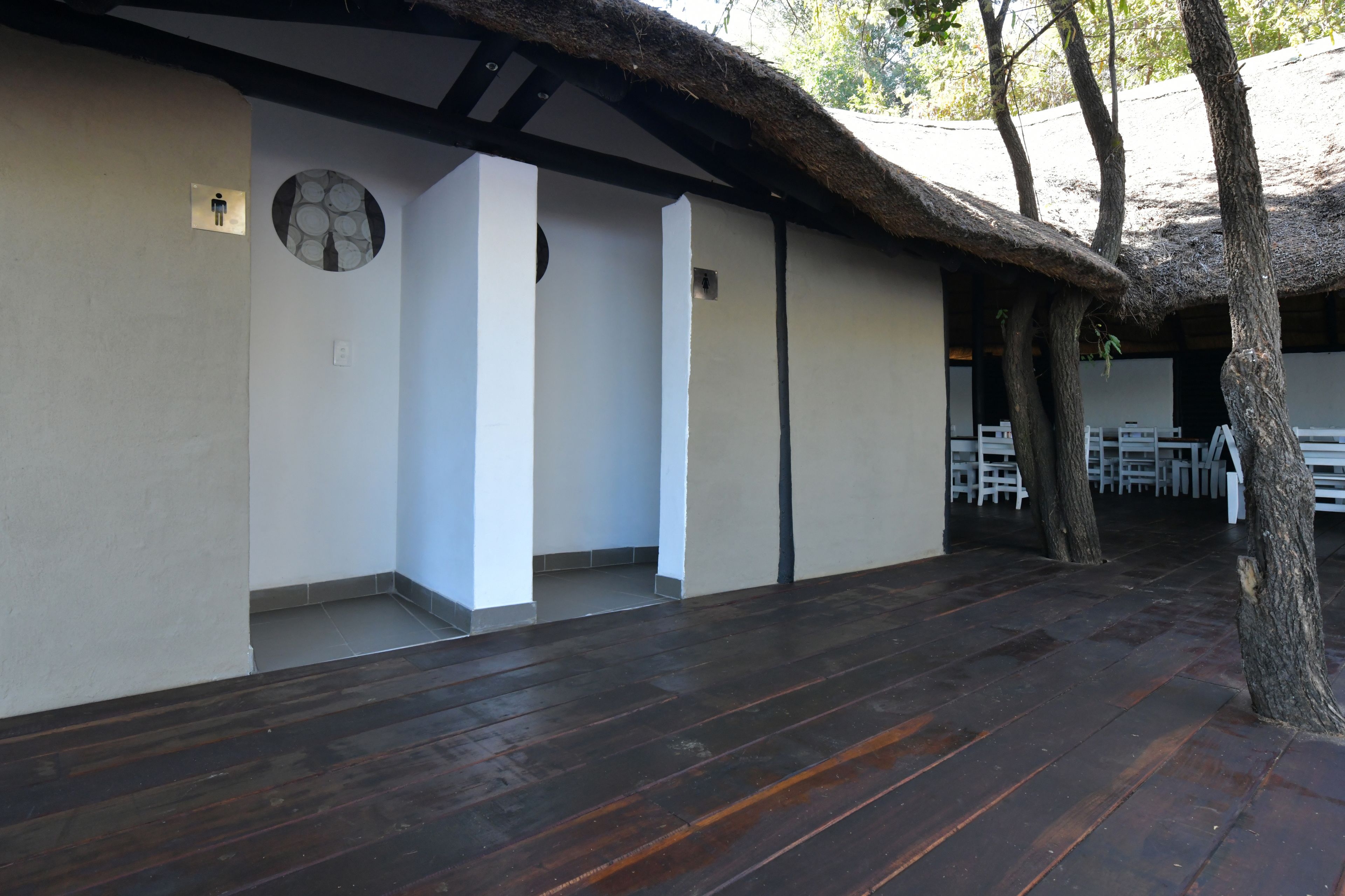 Un espacio al aire libre cubierto con techo de paja, suelo de madera y zona de estar con mesas y sillas.