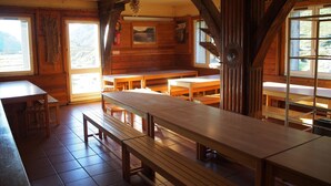 A rustic wooden cabin with multiple wooden benches and tables, large windows, and a fireplace. - Refuge des étangs de Bassiès - Hostel (Auzat)