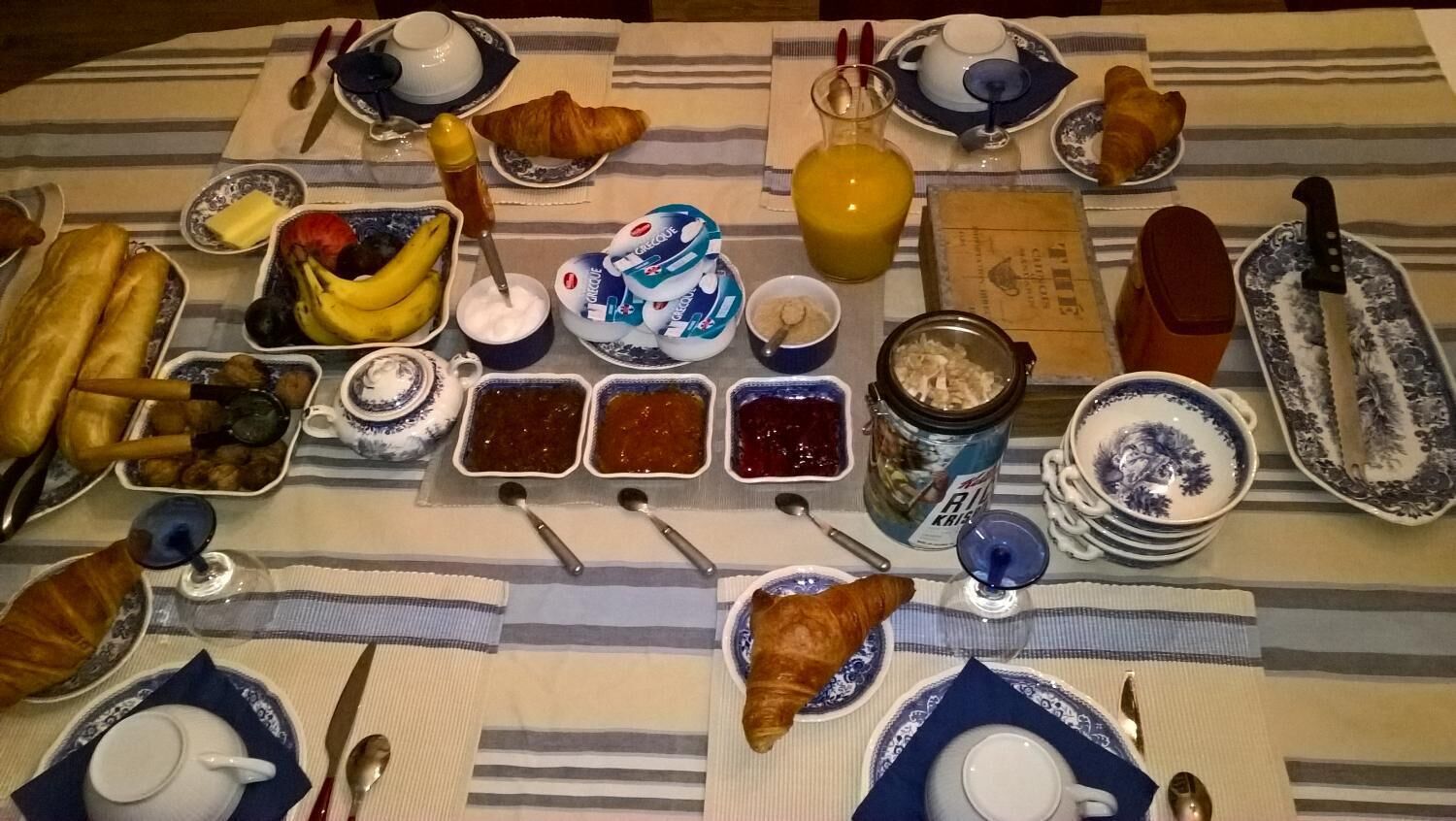 A breakfast table with croissants, fruit, yogurt, jams, and a bottle of juice.