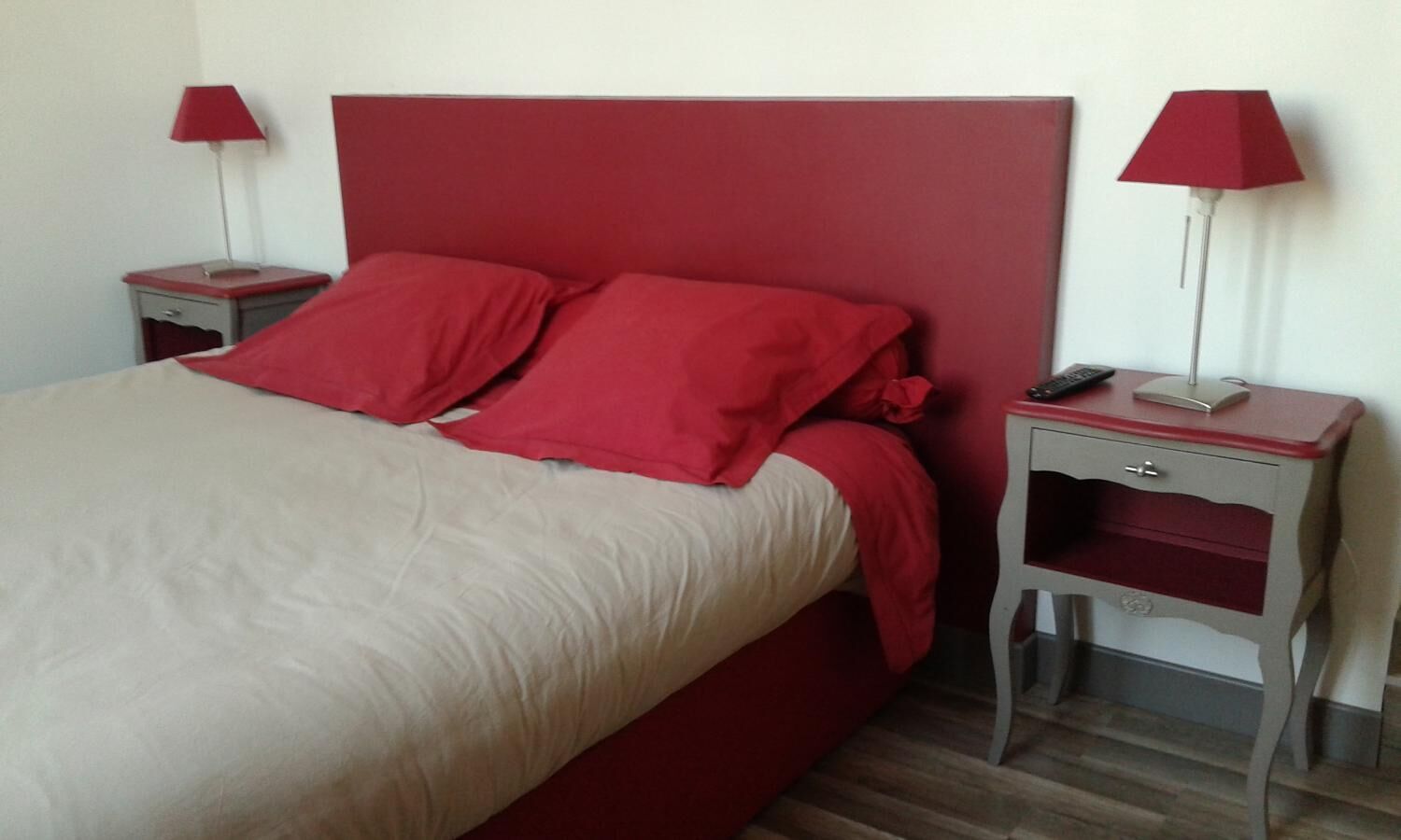 A bed with red bedding, two bedside tables with lamps, and a red headboard.