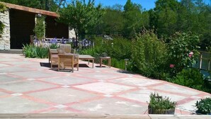 Una piscina de blau clar amb una zona de terrassa de pedra, mobles de fusta i vegetació abundant.