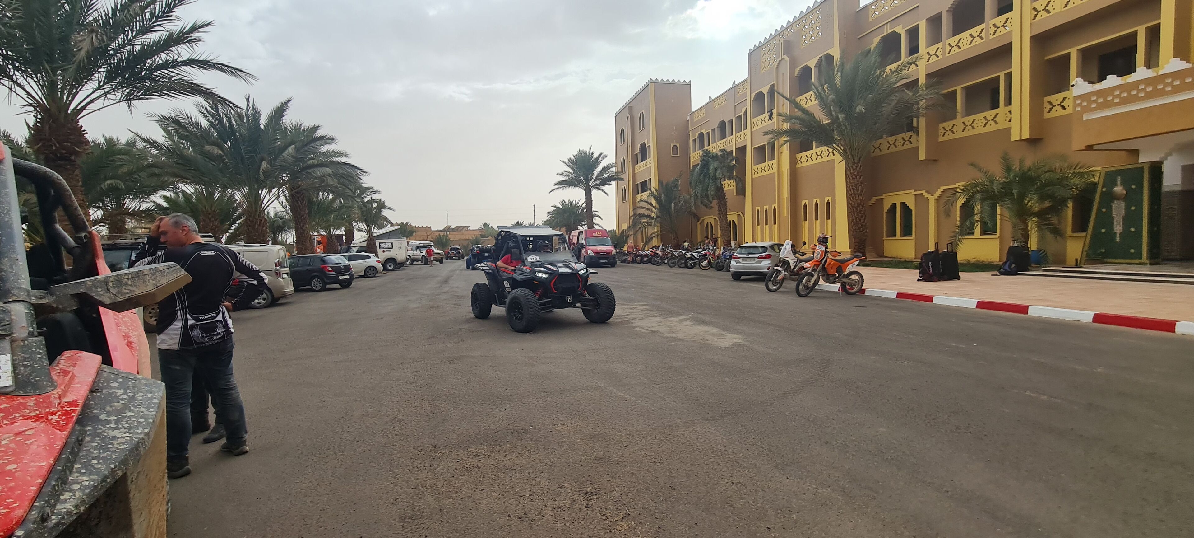 Calle con vehículos estacionados y un edificio con balcones y palmeras.