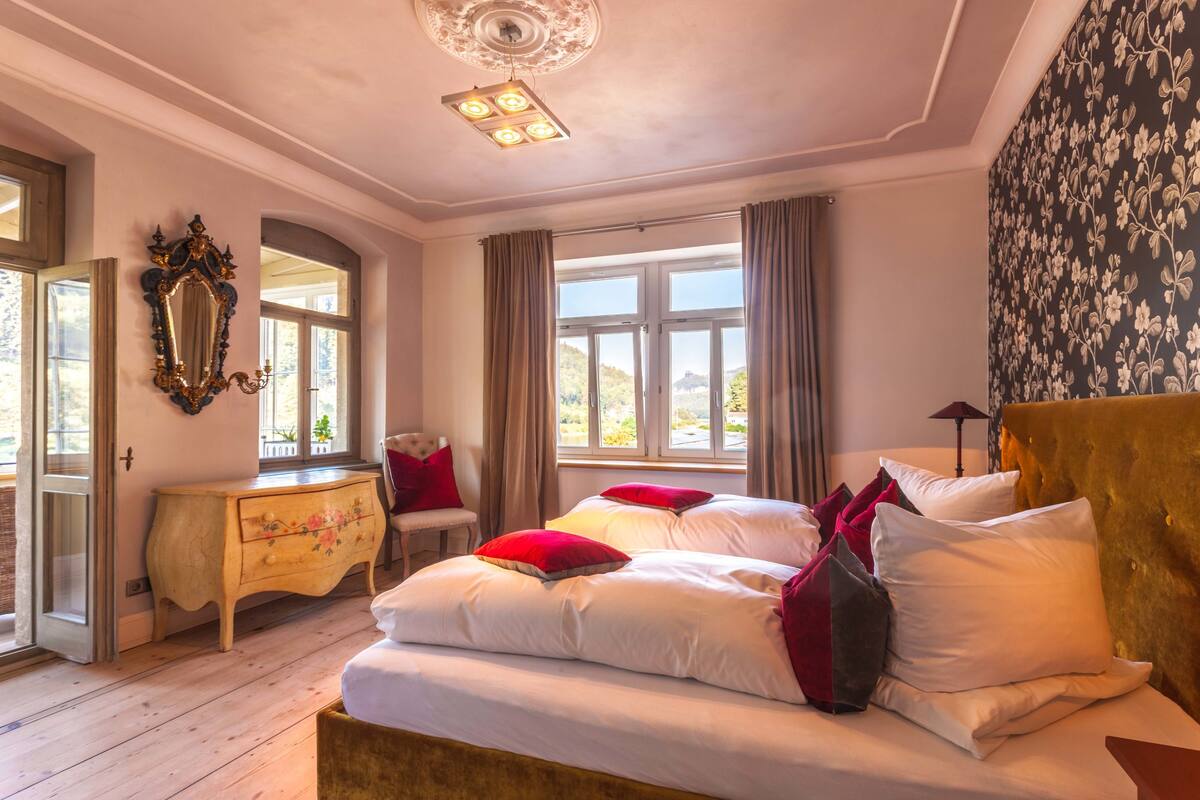 Quarto com cama grande, cômoda, cadeira e janela com cortinas.