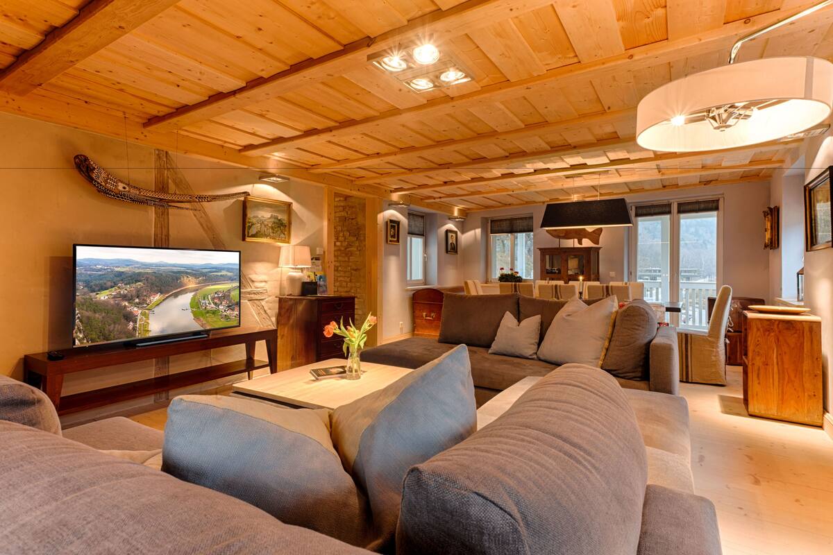 Uma sala de estar moderna com televisão de tela plana, assentos confortáveis, parede de destaque em pedra e vista para o exterior.