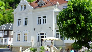 Valkoinen rakennus, jossa on kellotorni, ja jonka nimi on ”Villa Thunelöda”. Siinä on useita ikkunoita ja portaikko, joka johtaa sisäänkäynnille.