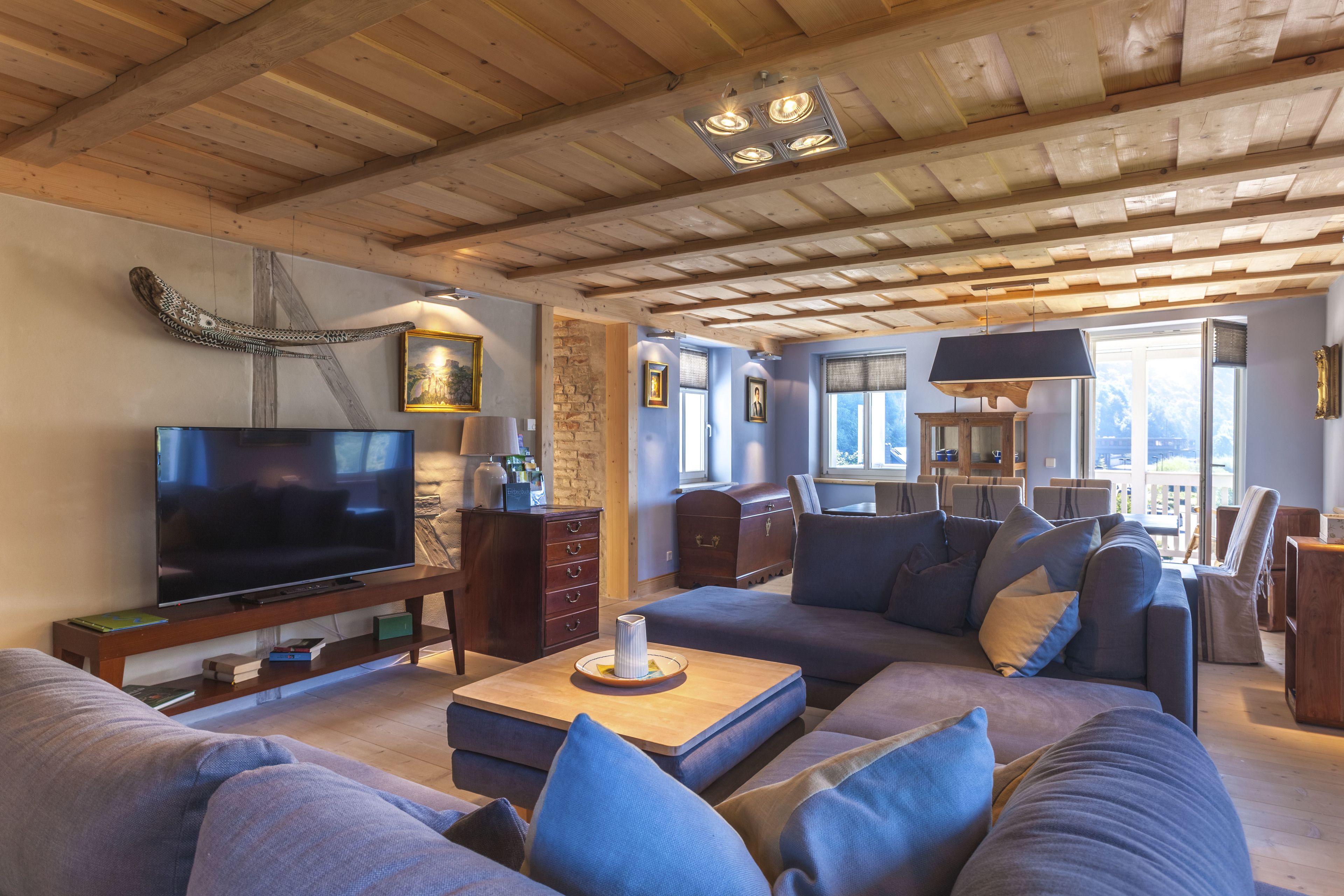 Un salón amplio con una televisión de pantalla plana grande, techo de madera y una zona de estar acogedora con sofás y cojines.