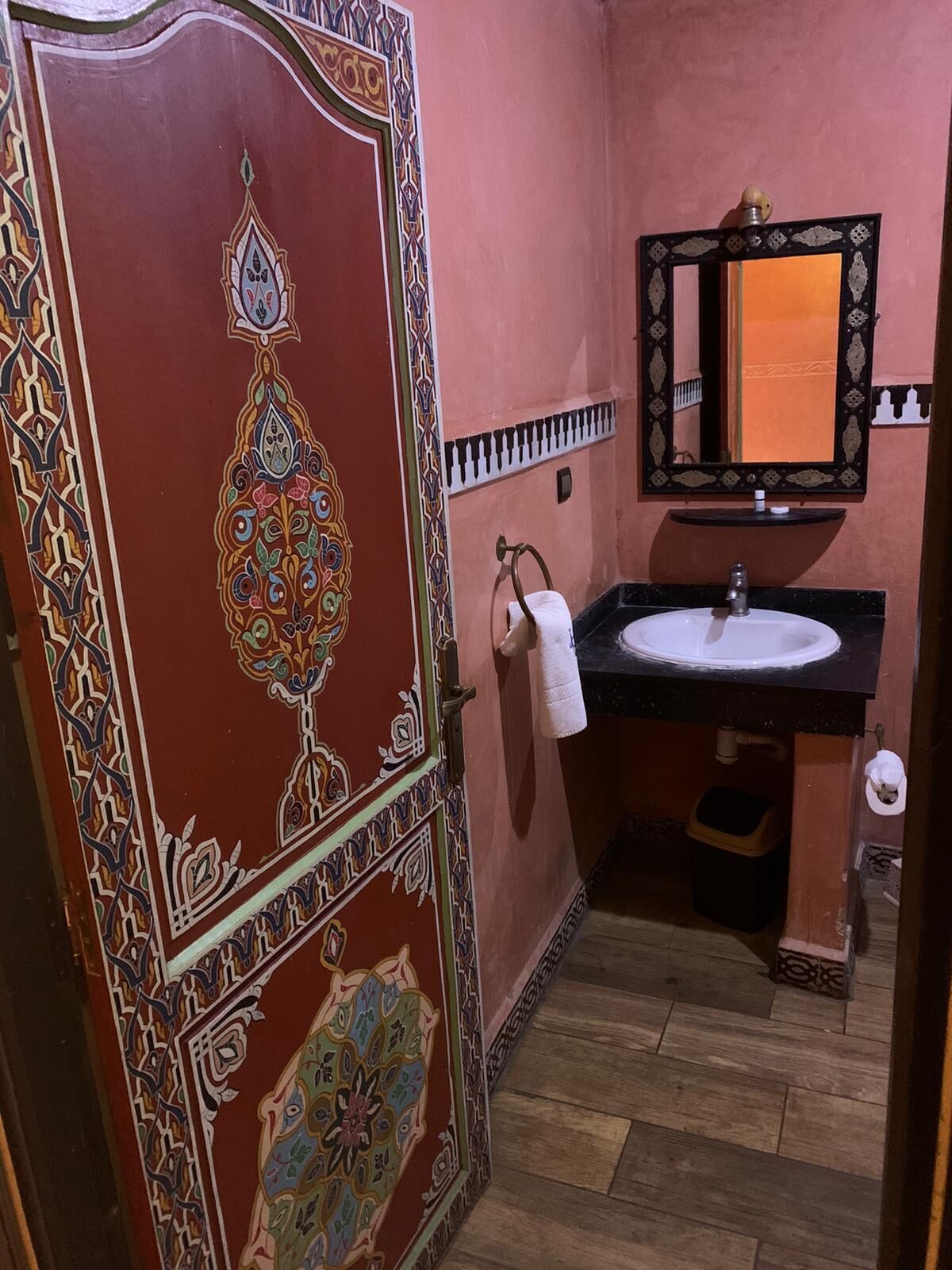 Um banheiro com porta decorativa, pia com espelho e toalha pendurada na parede.