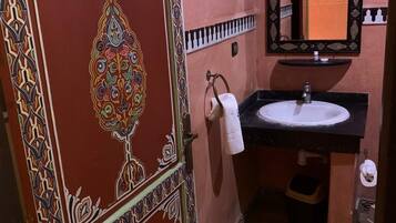 Um banheiro com porta decorativa, pia com espelho e toalha pendurada na parede.