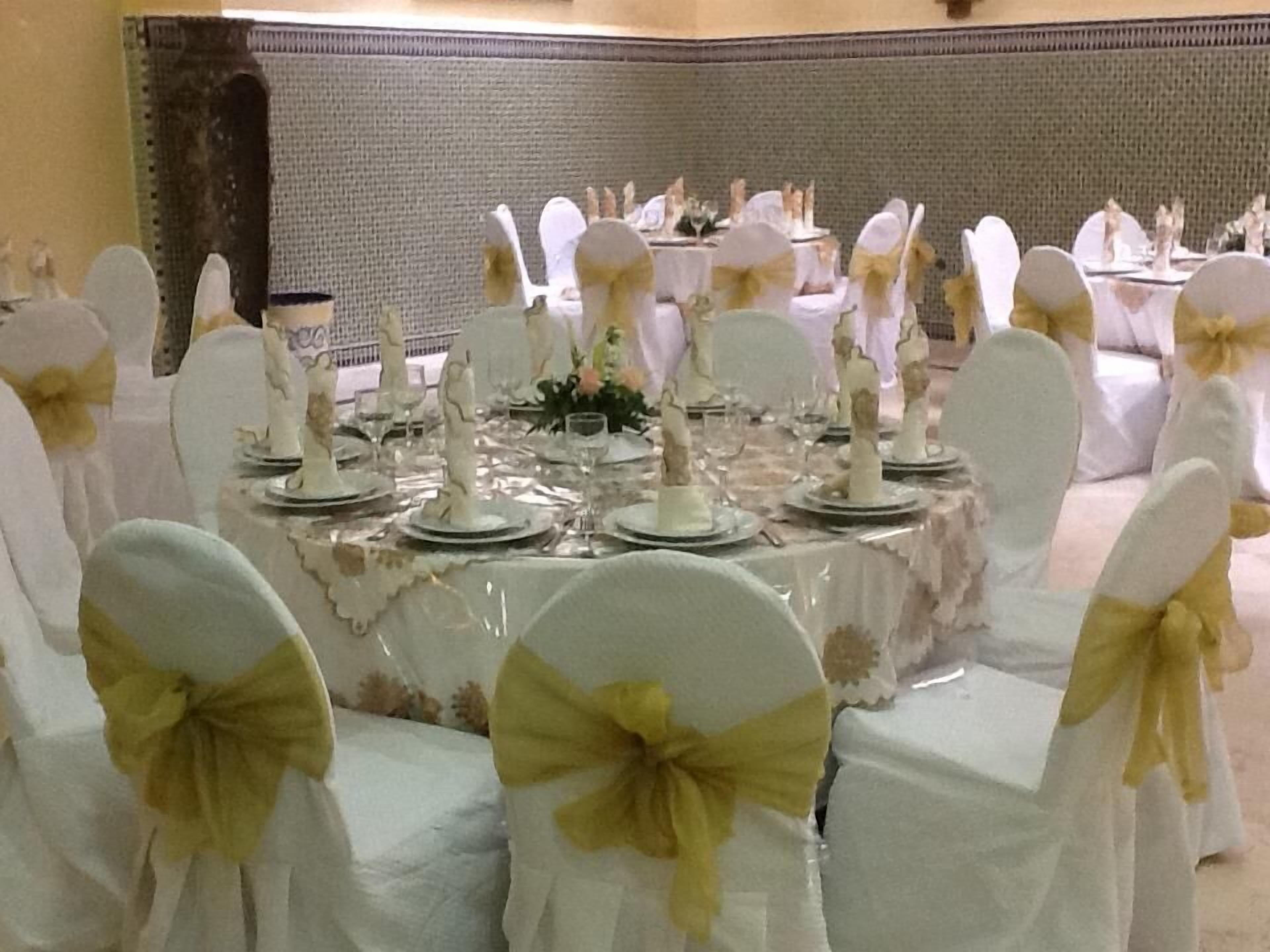 A banquet hall with round tables set for a formal event, each with white tablecloths and gold sashes on the chairs.