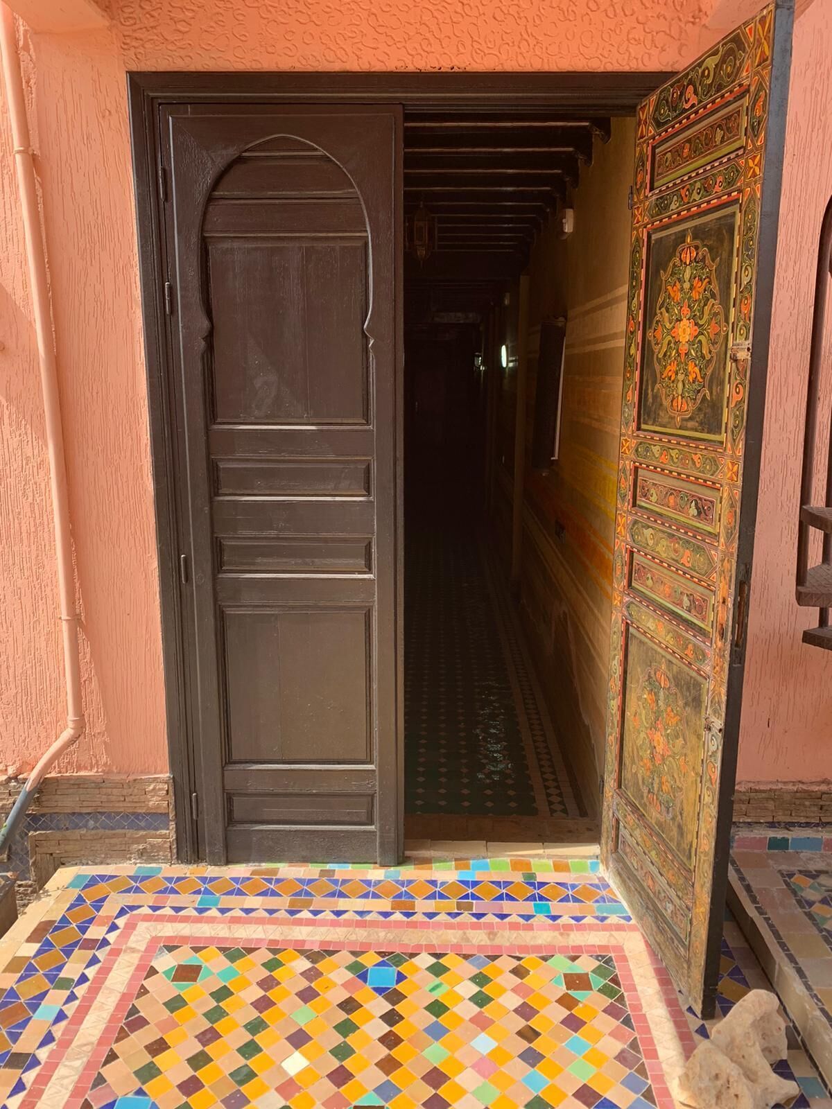 A traditional Moroccan door with intricate designs, leading into a hallway with patterned tiles.