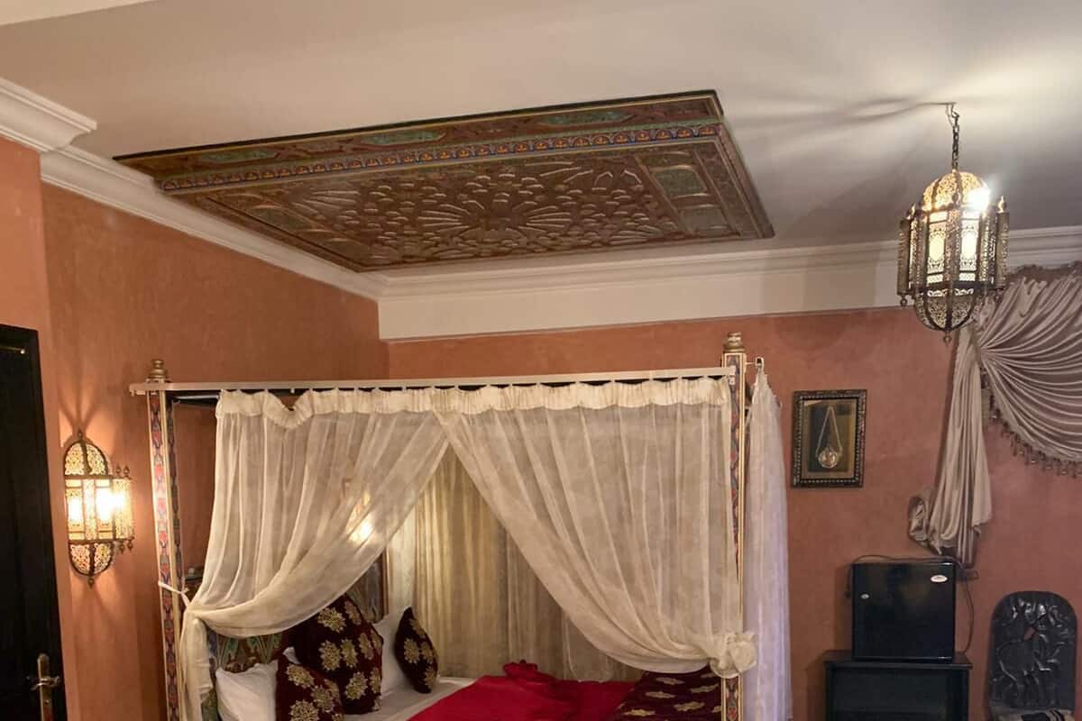 Quarto tradicional com cama de dossel, tapetes ornamentados e teto decorativo.