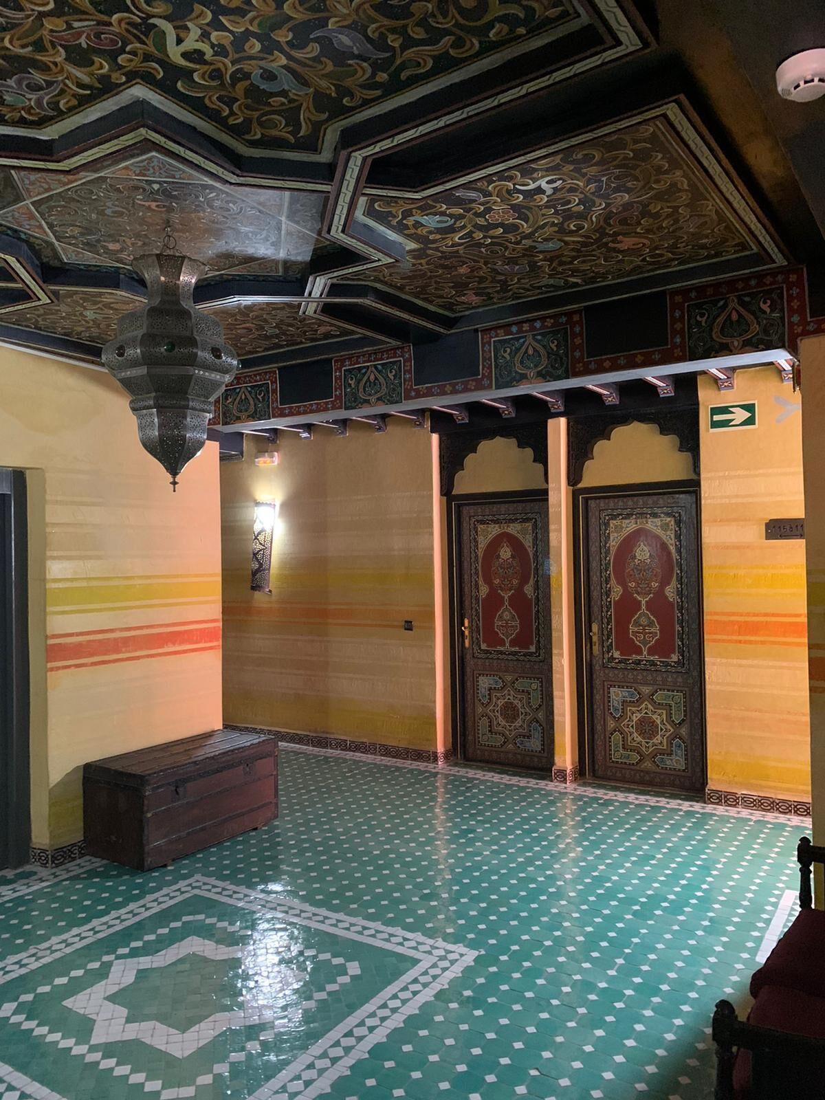 A room with a patterned floor, ornate doors, and a hanging light fixture.