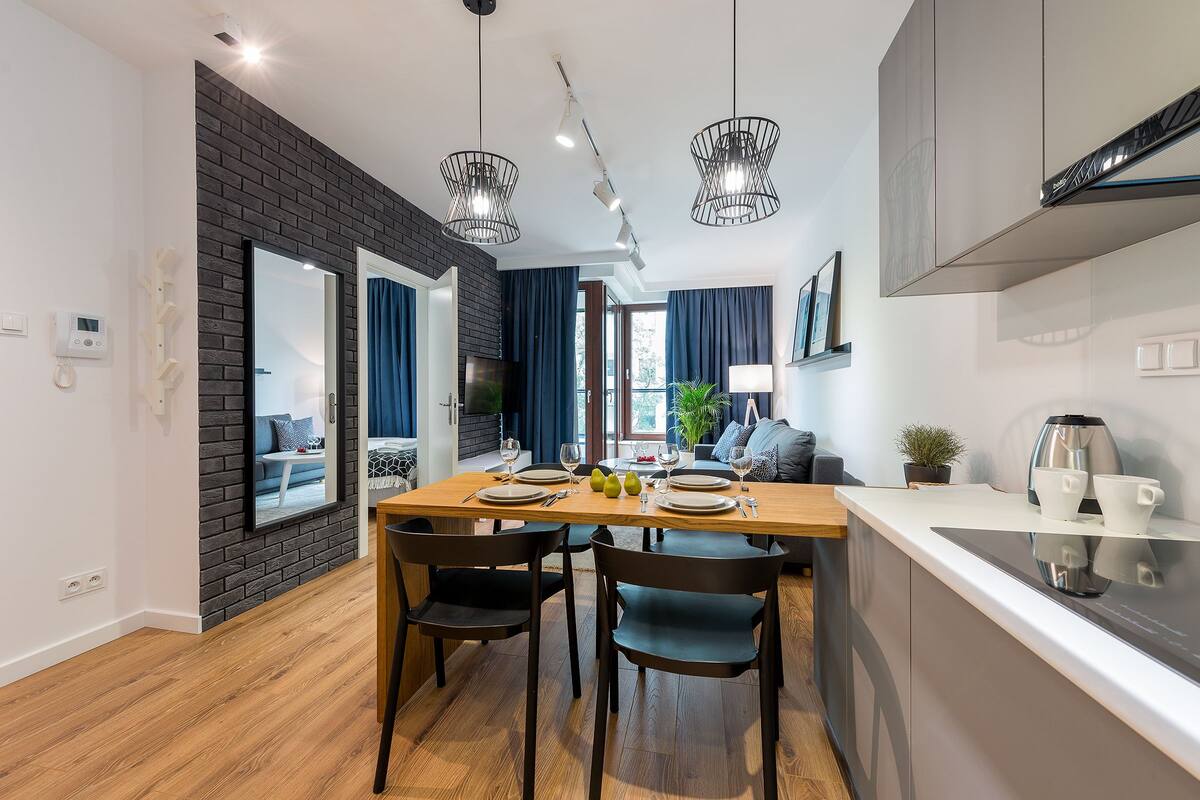 Une cuisine moderne avec une table à manger en bois, des chaises noires et des luminaires suspendus.