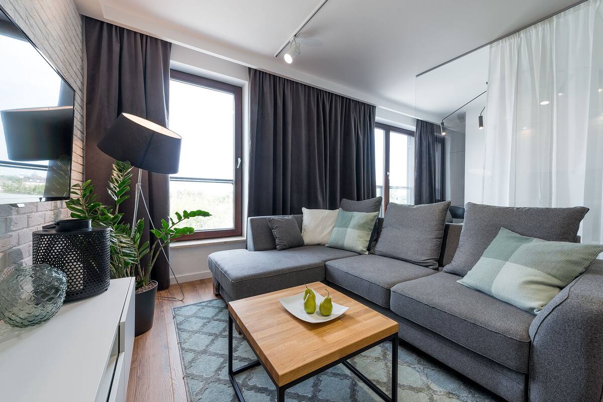 Un salon moderne avec un canapé gris, une table basse en bois et un téléviseur posé sur un meuble blanc.