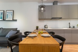 Una cocina moderna con armarios grises, una mesa de comedor de madera preparada para cuatro comensales y una lámpara colgante.