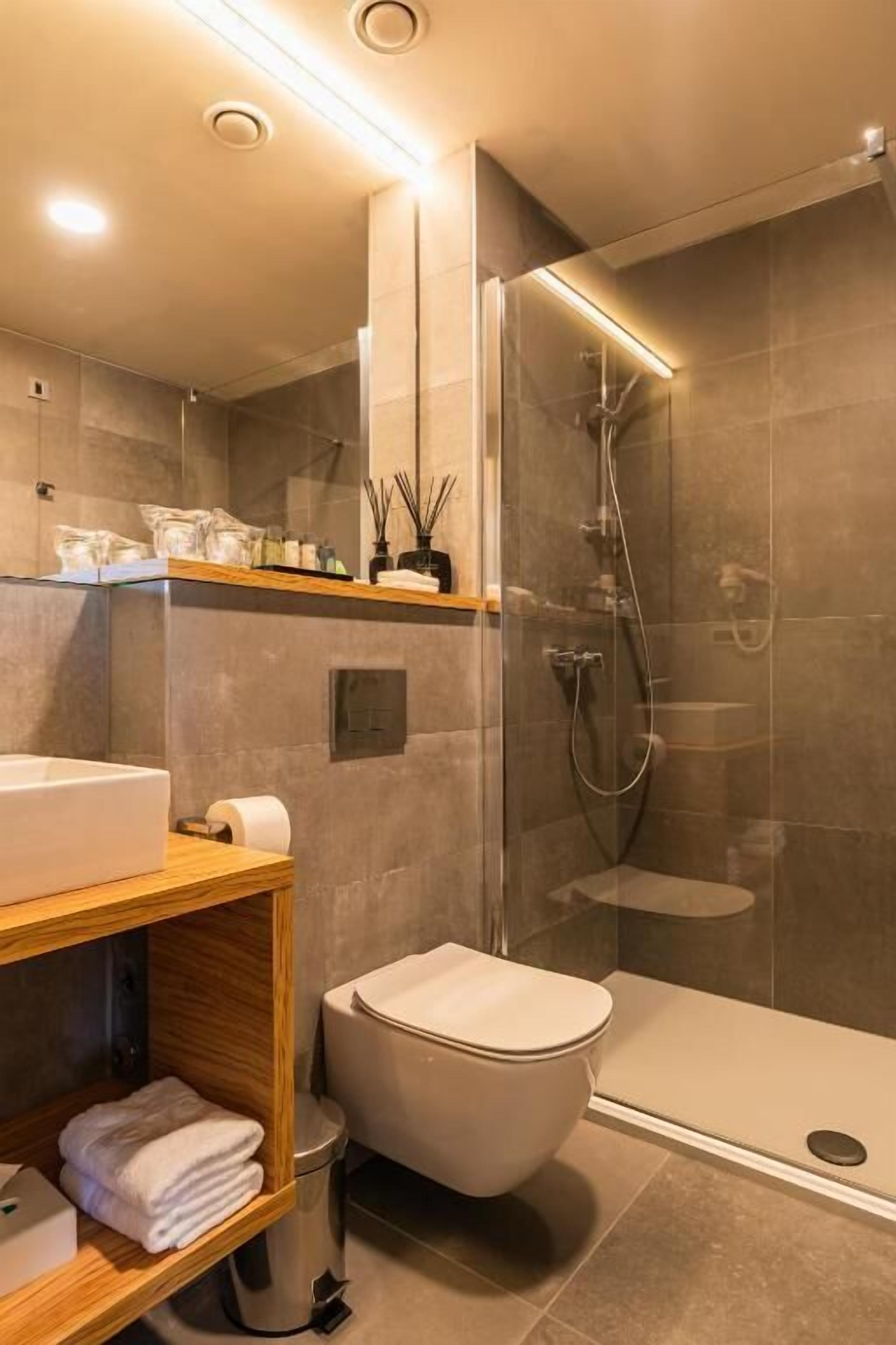 Un baño moderno con cabina de ducha de vidrio, tocador de madera y un inodoro.