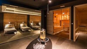 A modern spa room with a glass-enclosed sauna, massage chairs, and a central table with a beverage dispenser. - Hotel Olea (Novalja)