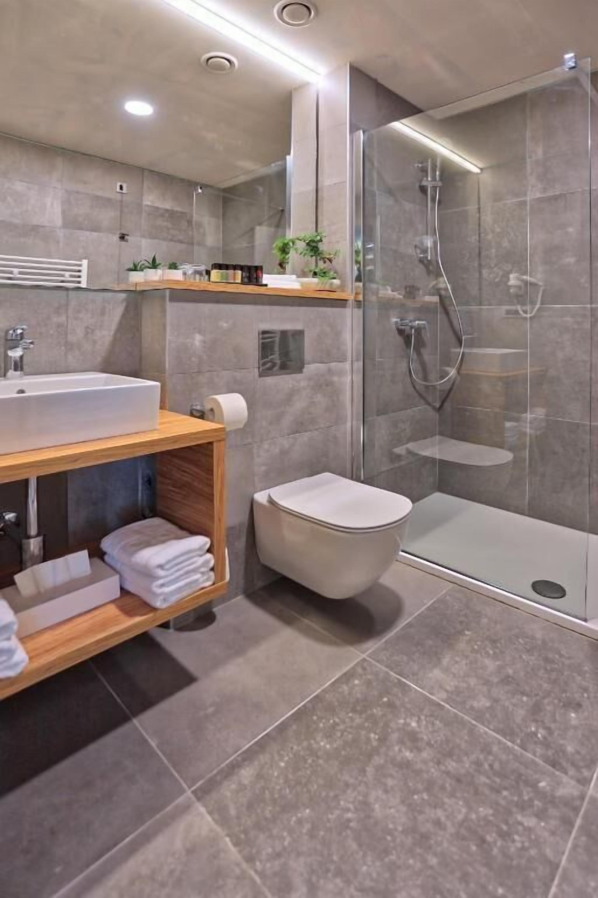 Un baño moderno con ducha de vidrio, tocador de madera con lavamanos y un inodoro.