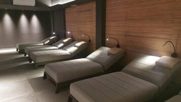 A row of massage chairs in a dimly lit room with wooden panel walls and a ceiling-mounted air conditioning unit.